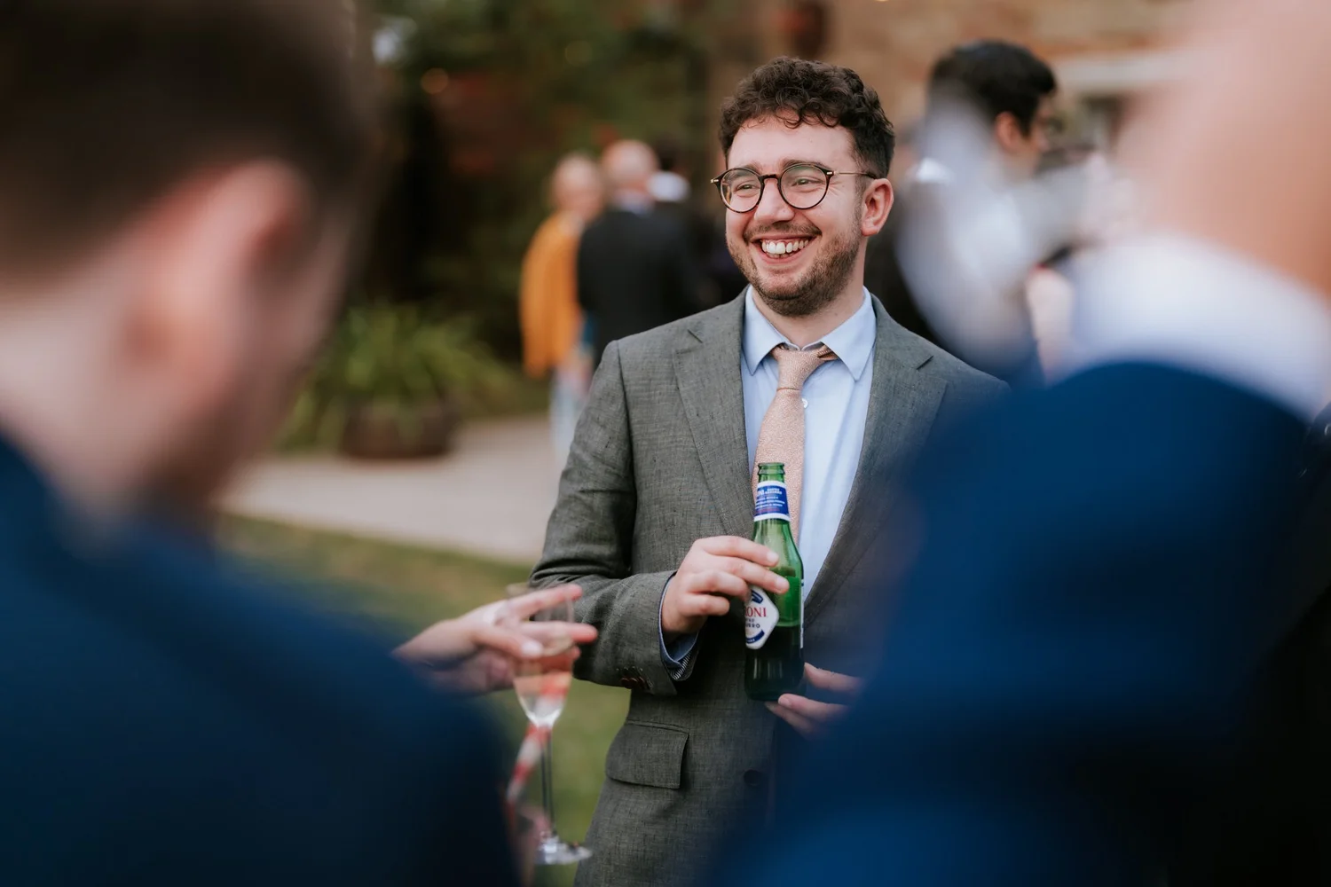 A guest wearing glasses and a grey jacket smiles while chatting over a drink outside.