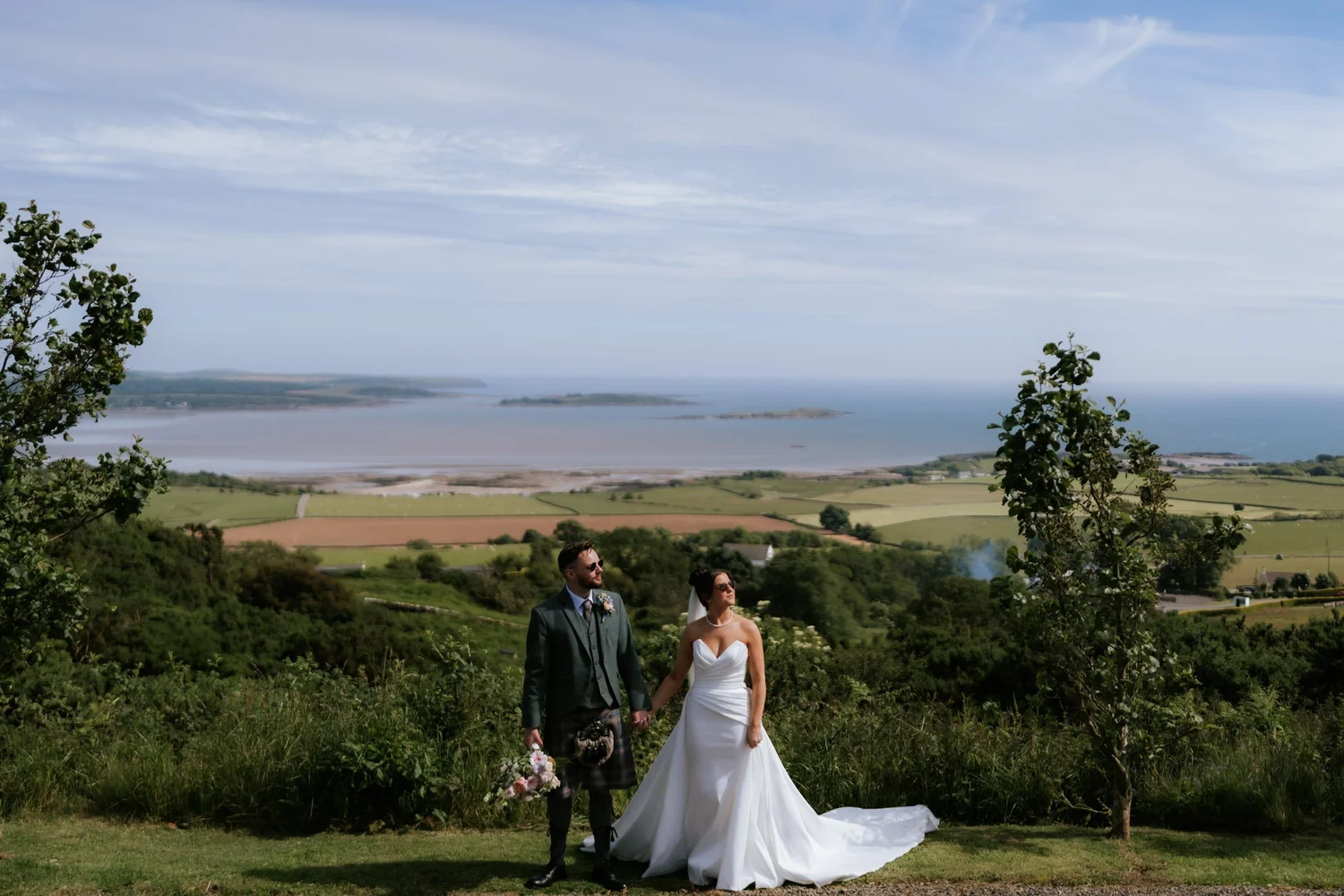 Lois and Dougie holding hands at GG’s Yard with green fields and the Galloway coast stretching out behind them.