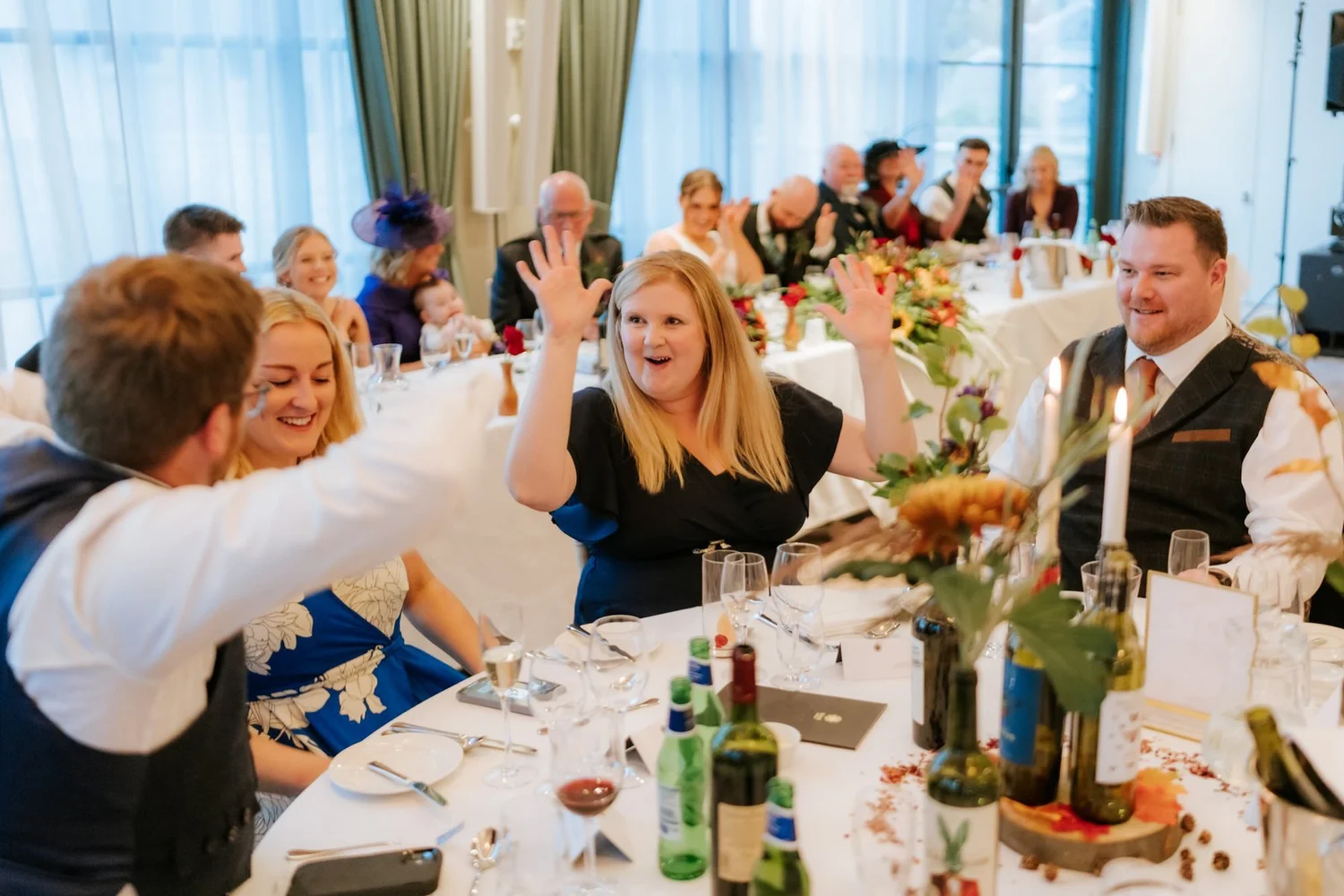 Guests joining in around a reception table, with a woman raising her hand and laughing.