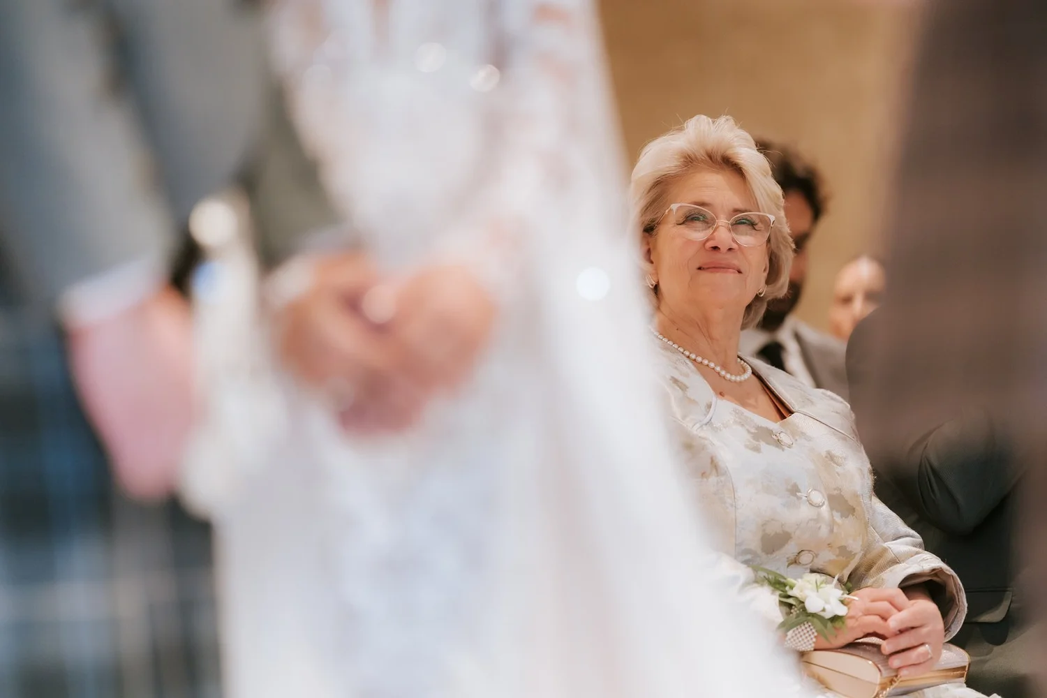 A wedding guest watching Cristina and Connor during their ceremony, with the couple’s joined hands in the foreground.