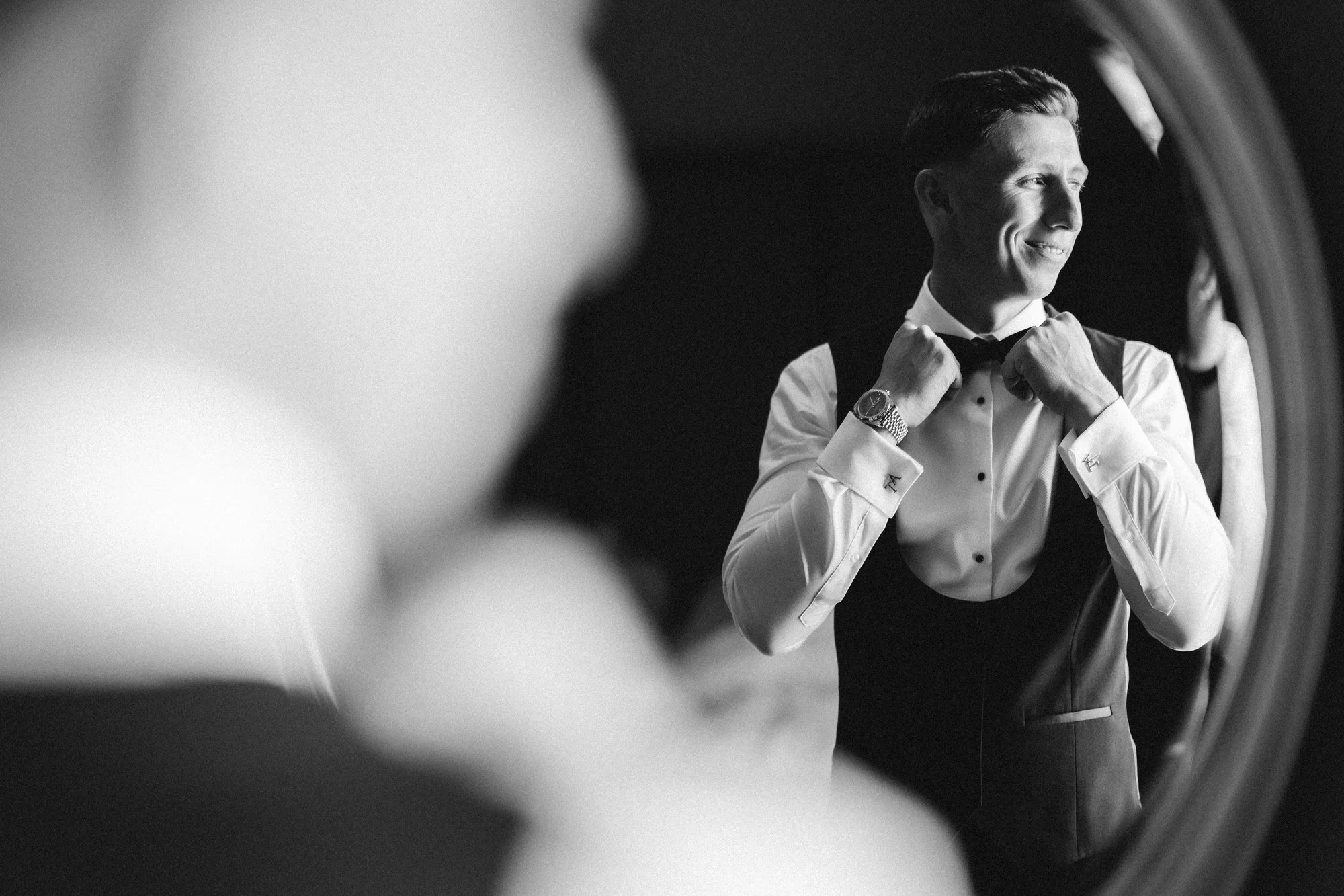 Black-and-white photograph of Aiden adjusting his bow tie in the mirror.