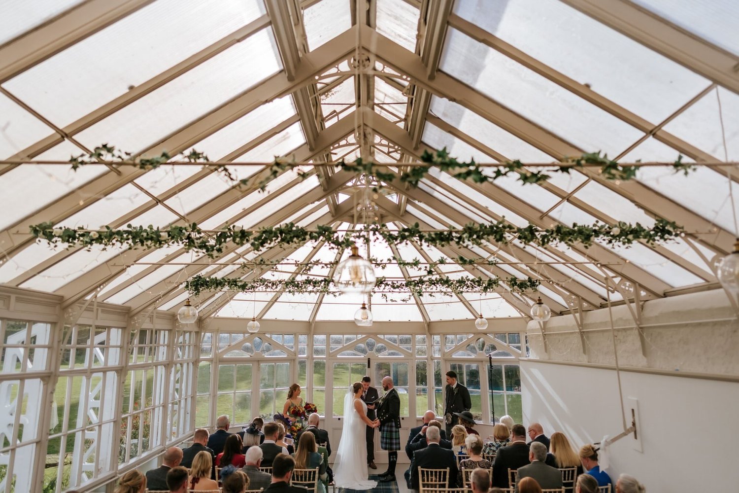 A wide view beneath the conservatory’s glass roof during Kendall and Ewen’s wedding ceremony.