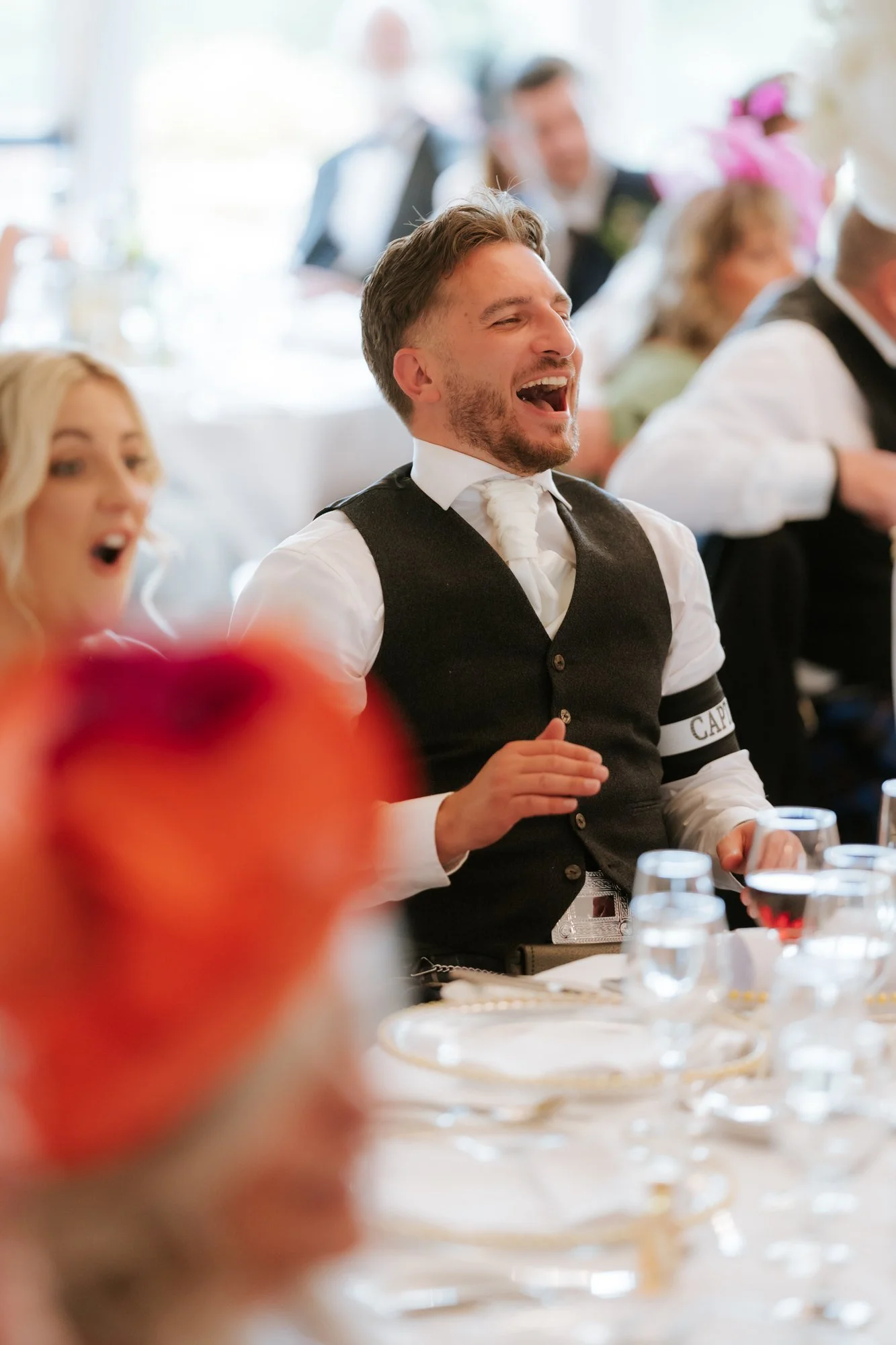 A wedding guest wearing a captain armband laughing at his table at Glenbervie House.