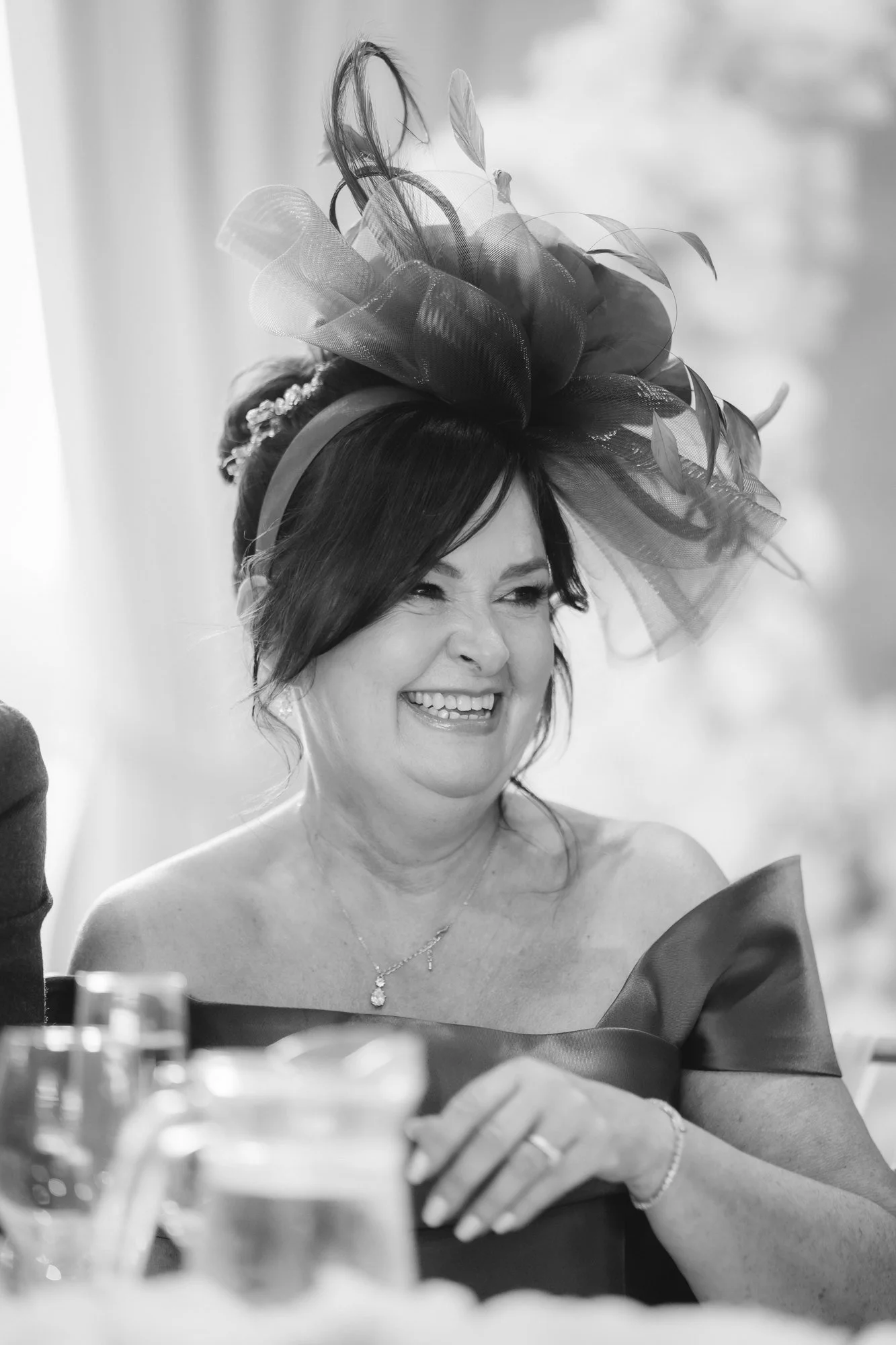 Black-and-white portrait of a smiling guest wearing a large fascinator at Glenbervie House.