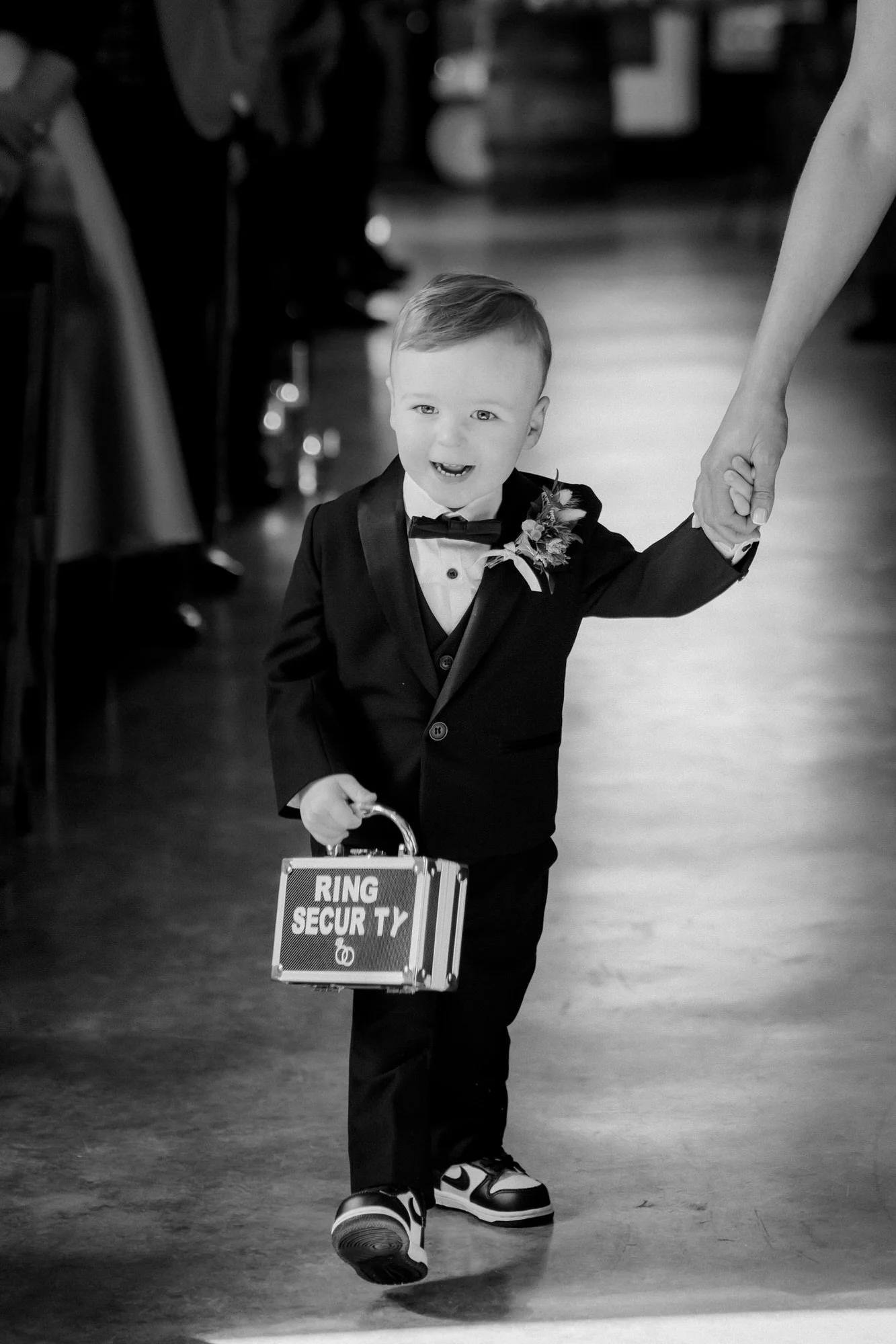 A young ring bearer carrying his case down the aisle, in black and white