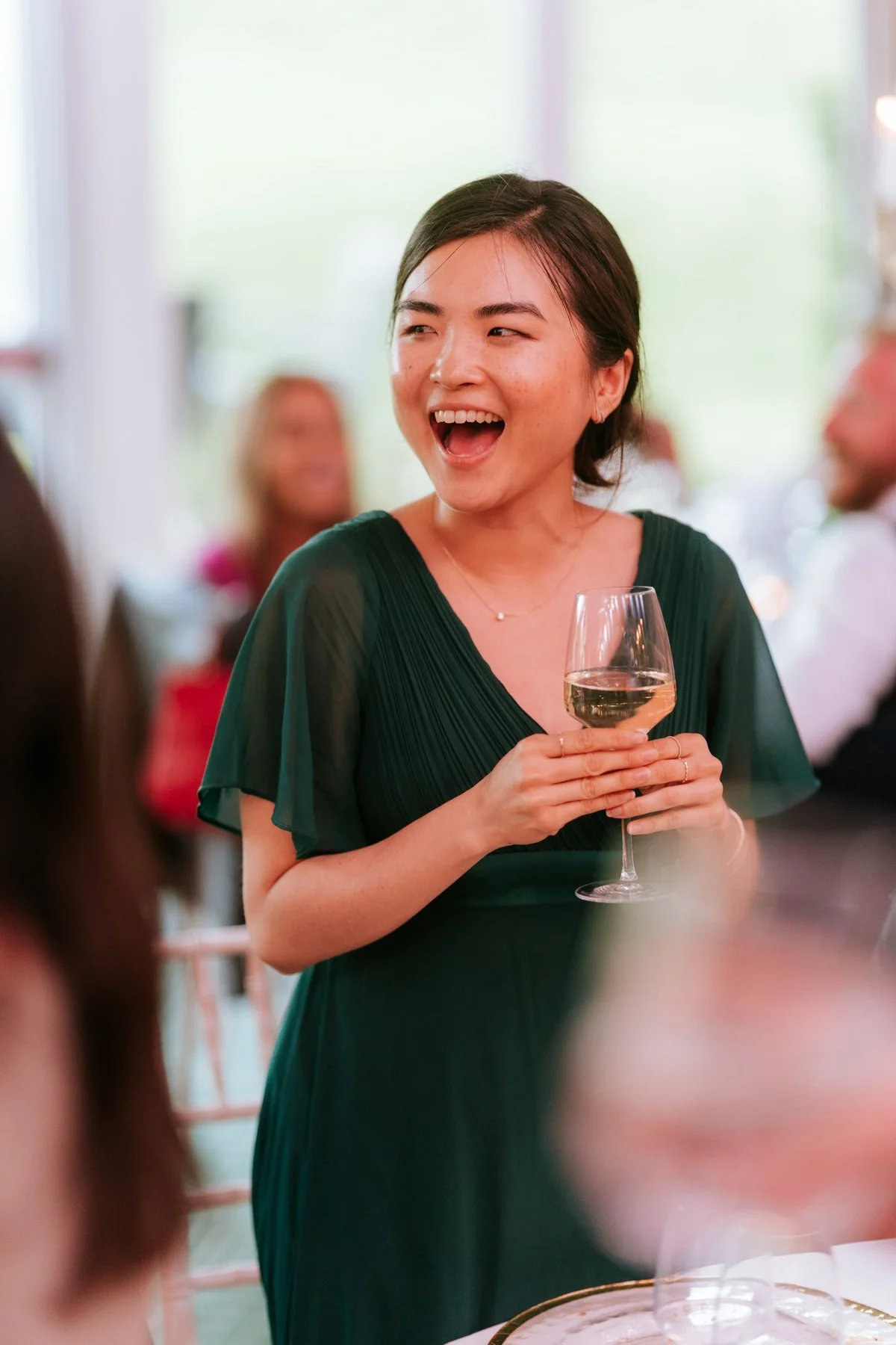 A bridesmaid in a green dress laughing with a glass in her hand during the wedding reception.