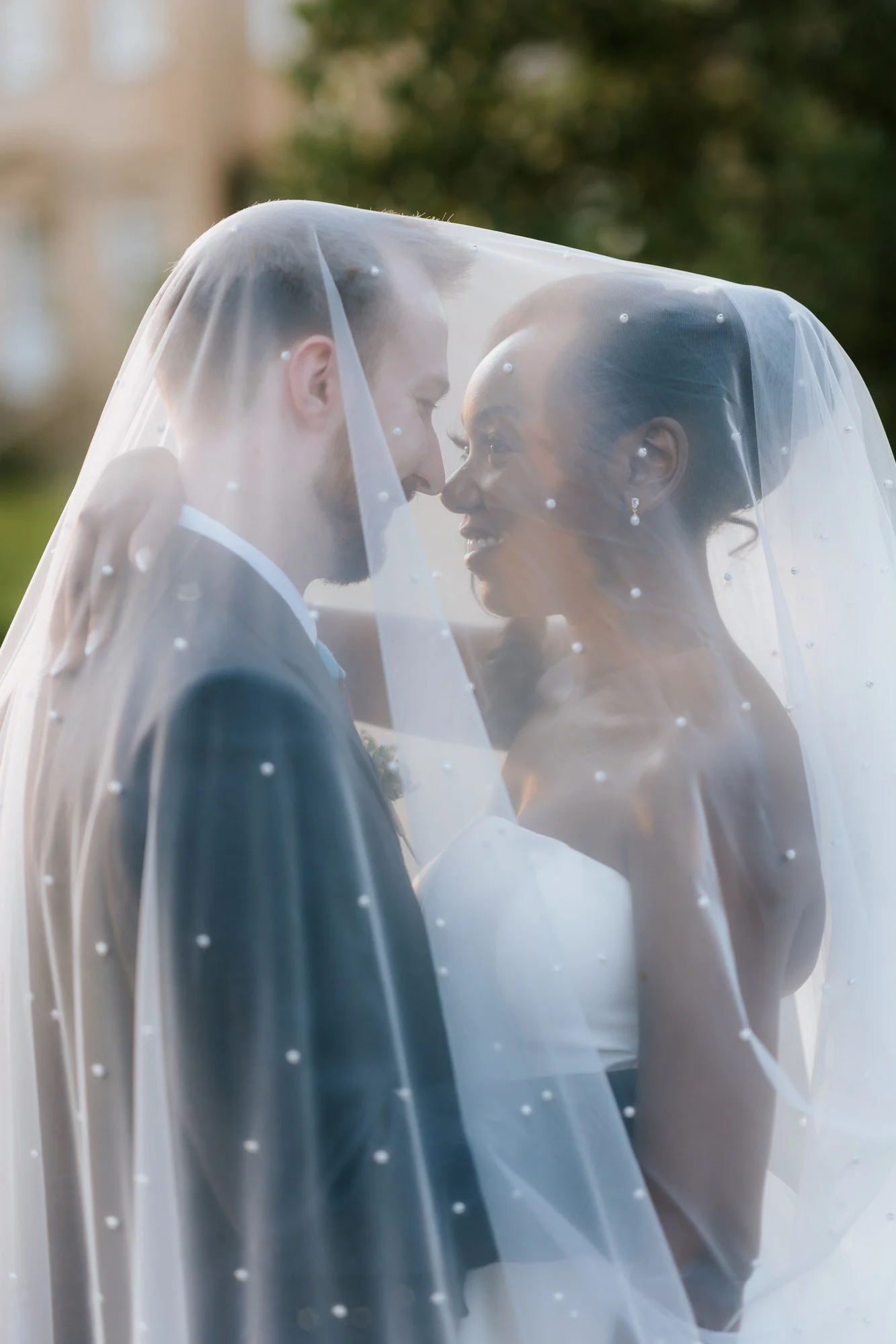 Kuda and Jamie smiling at each other beneath the veil.