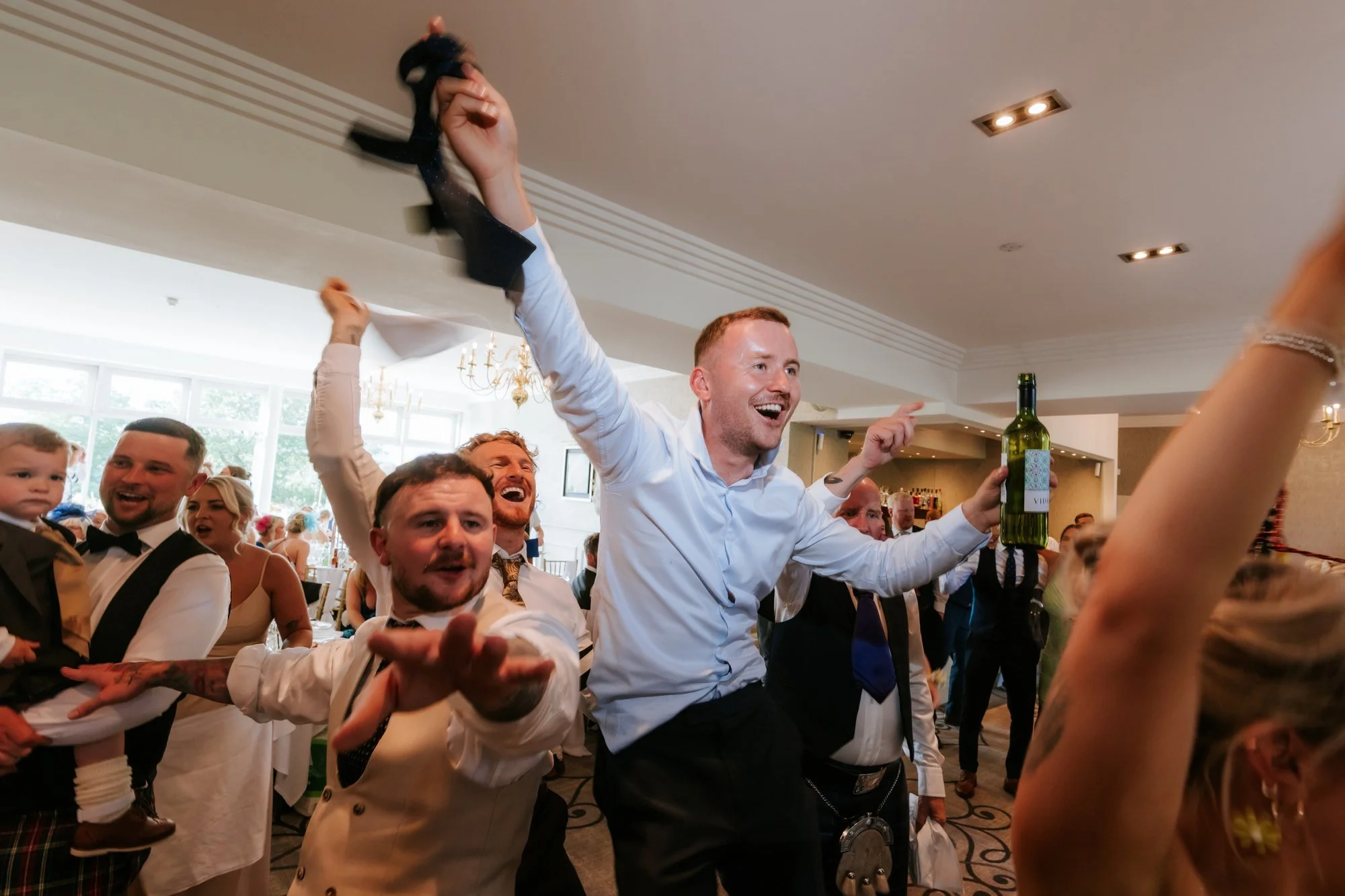 Wedding guests cheering with drinks and waving a tie in the air at Glenbervie House.