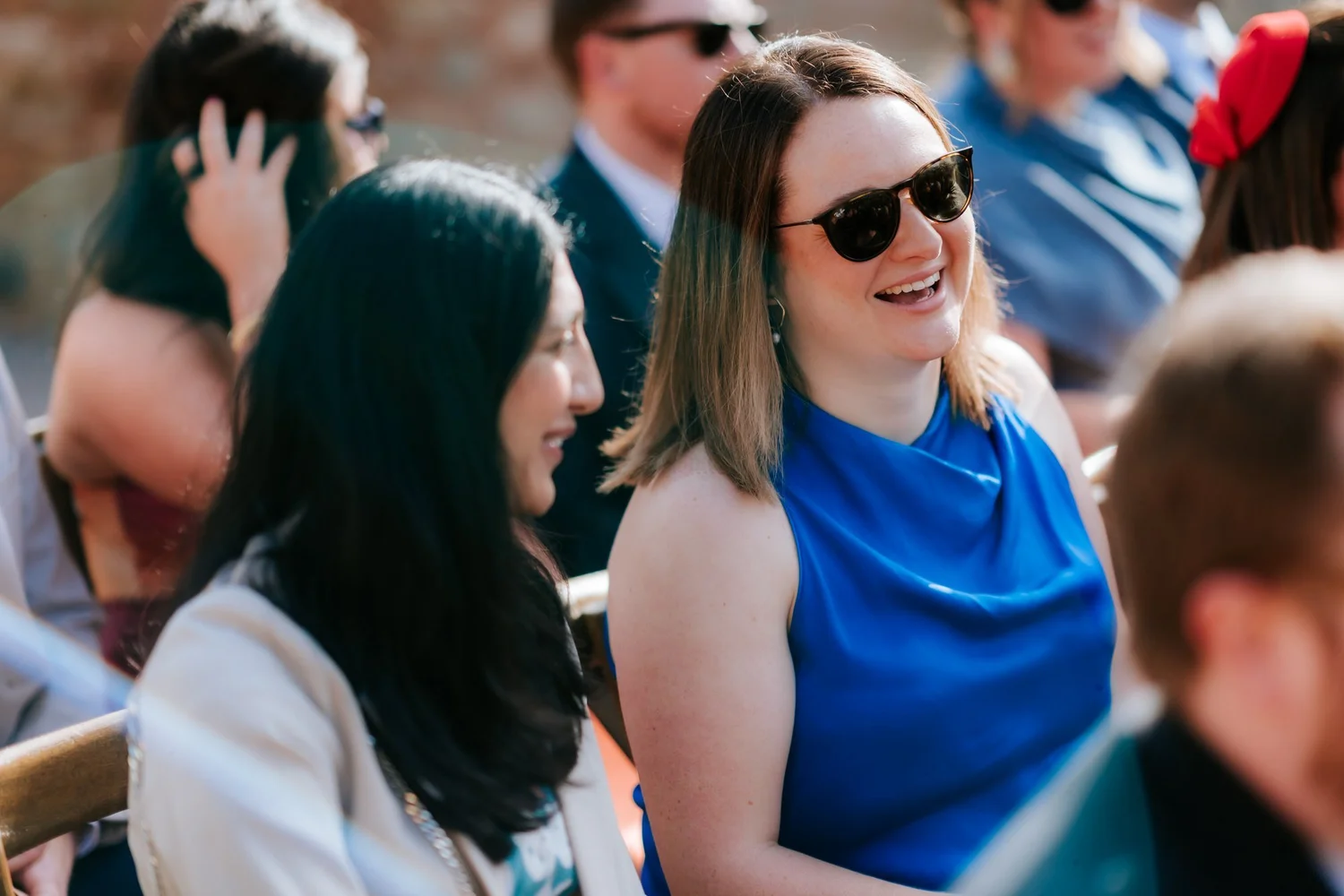 Two guests in sunglasses watch the ceremony, one wearing a bright blue dress.