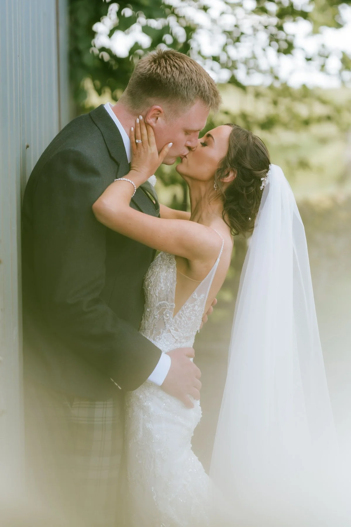 Lauren and Jamie sharing a kiss beside a window, framed by greenery.