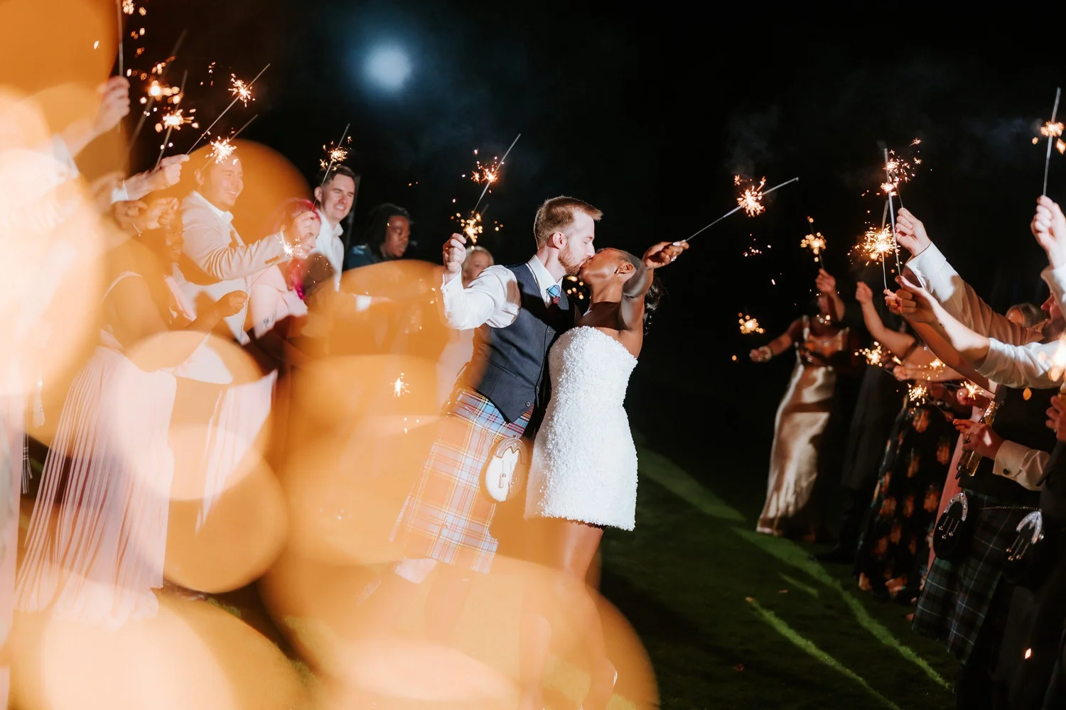 Kuda and Jamie sharing a sparkler kiss behind a golden foreground glow.