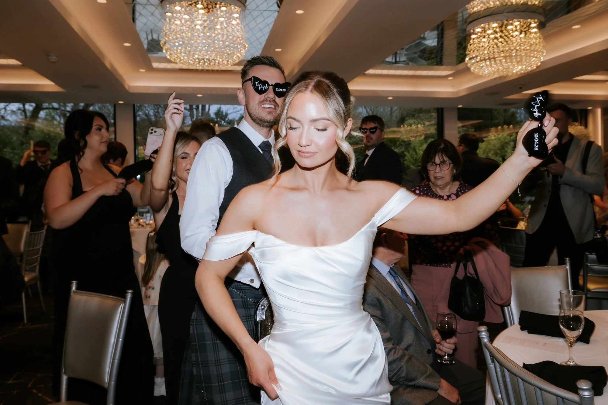 Elle dancing in front of Adam while holding heart-shaped sunglasses
