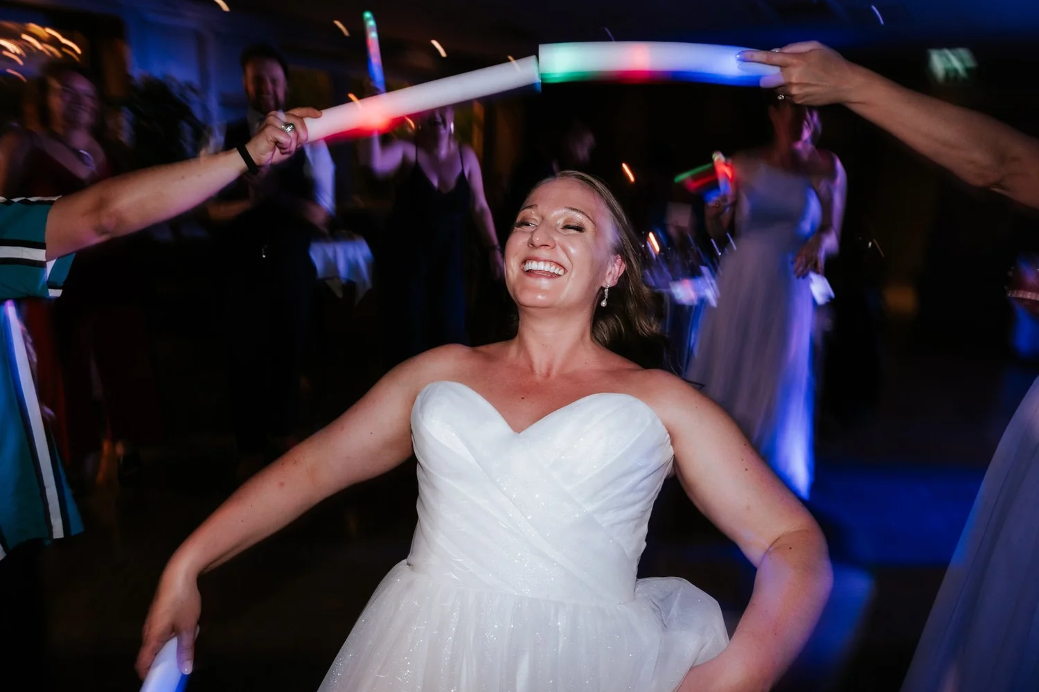 Allie dancing beneath colourful lights as guests wave glow sticks around her.