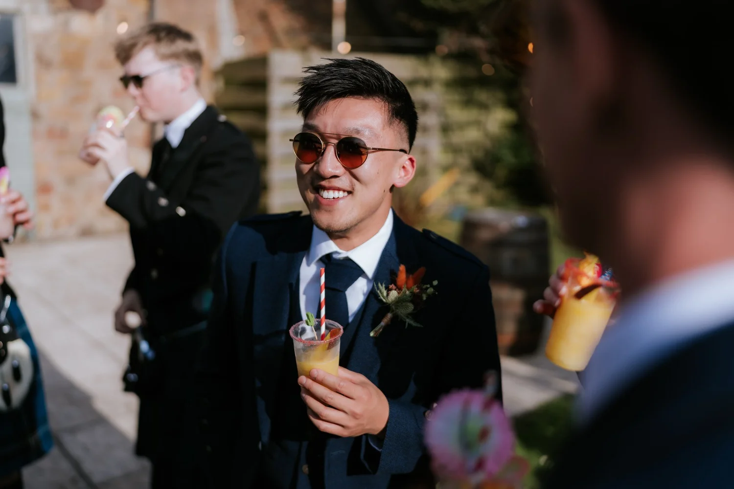 A guest in sunglasses and a dark waistcoat smiles during the drinks reception.