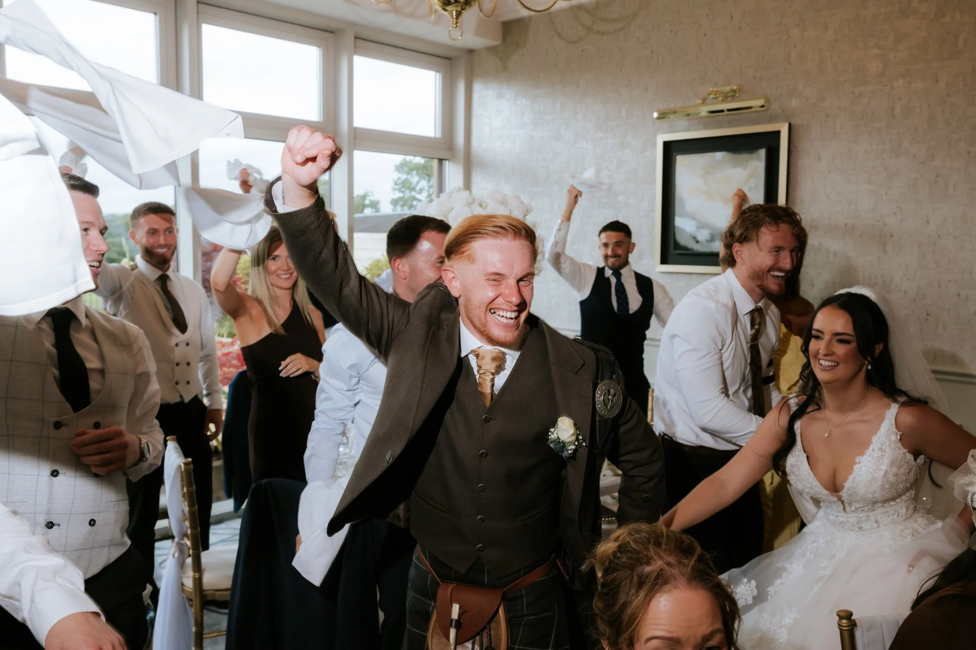 Scott raising his fist as wedding guests wave white napkins at Glenbervie House.
