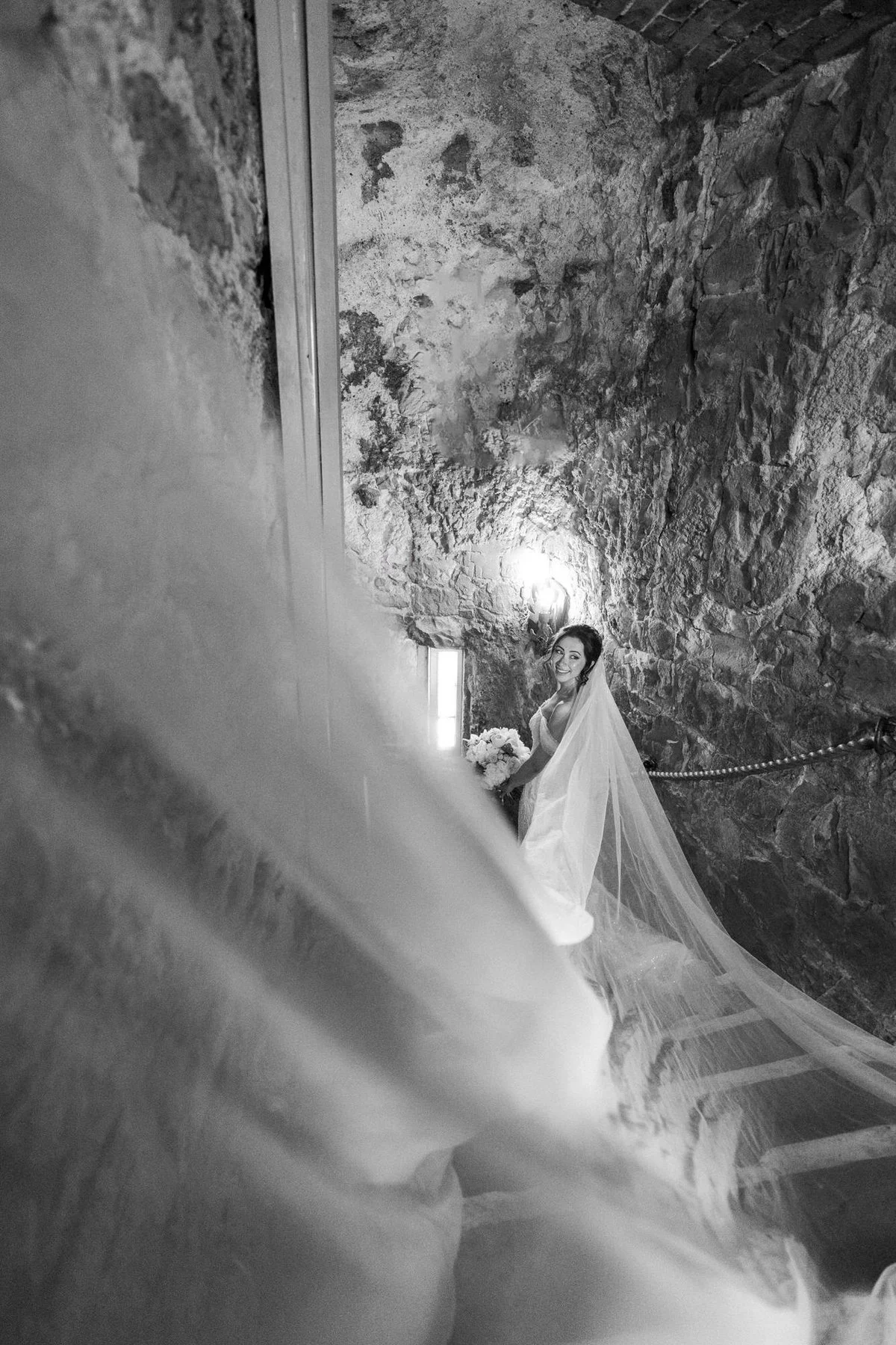 Black-and-white photograph of Kim on the narrow stone staircase inside the castle tower, with her veil trailing behind her.