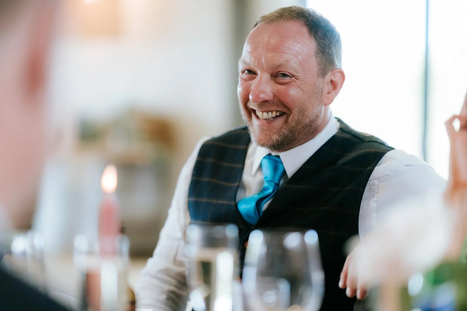 A guest in a waistcoat and blue tie smiling at the reception.