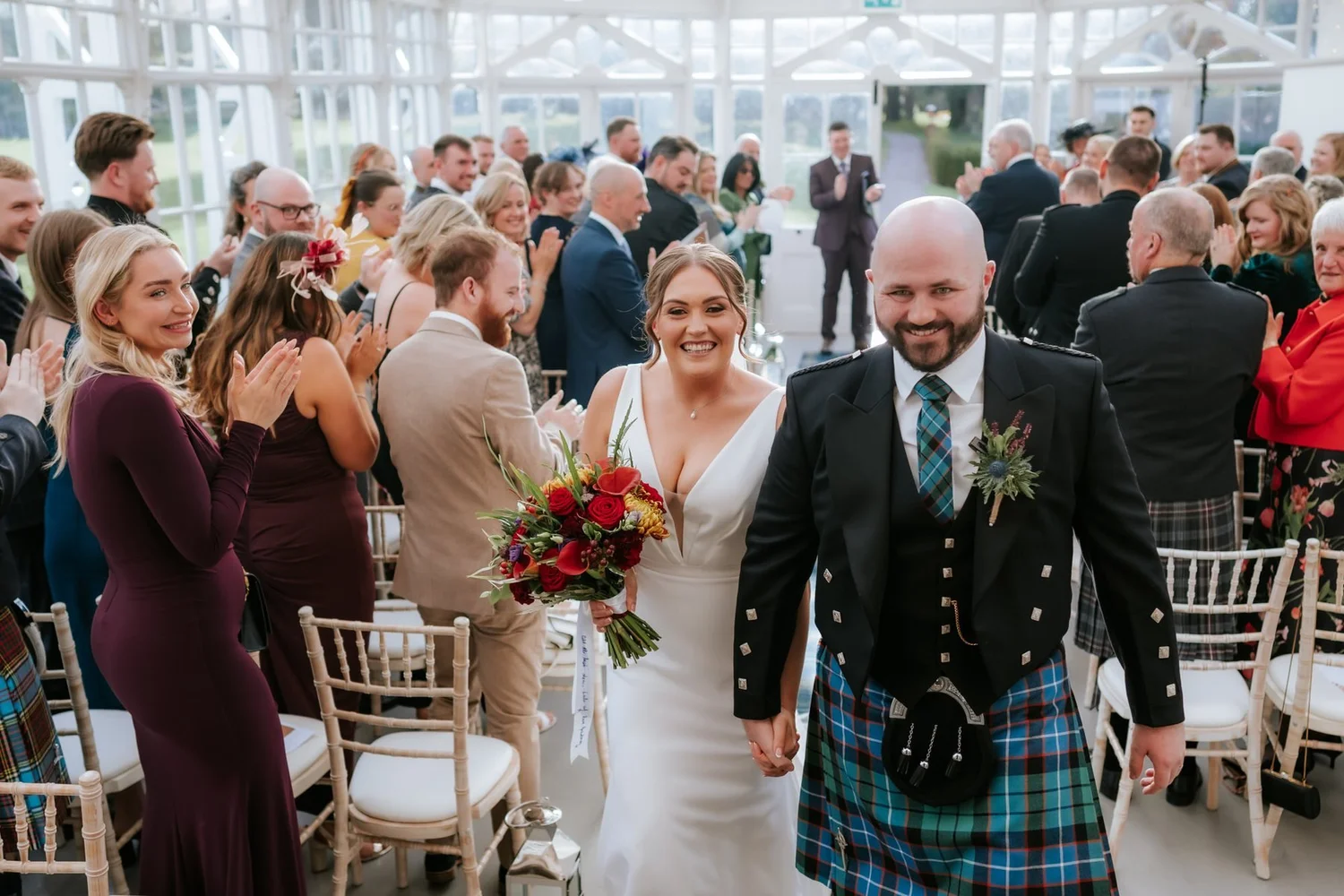 Kendall and Ewen walking through their smiling guests after the conservatory ceremony.