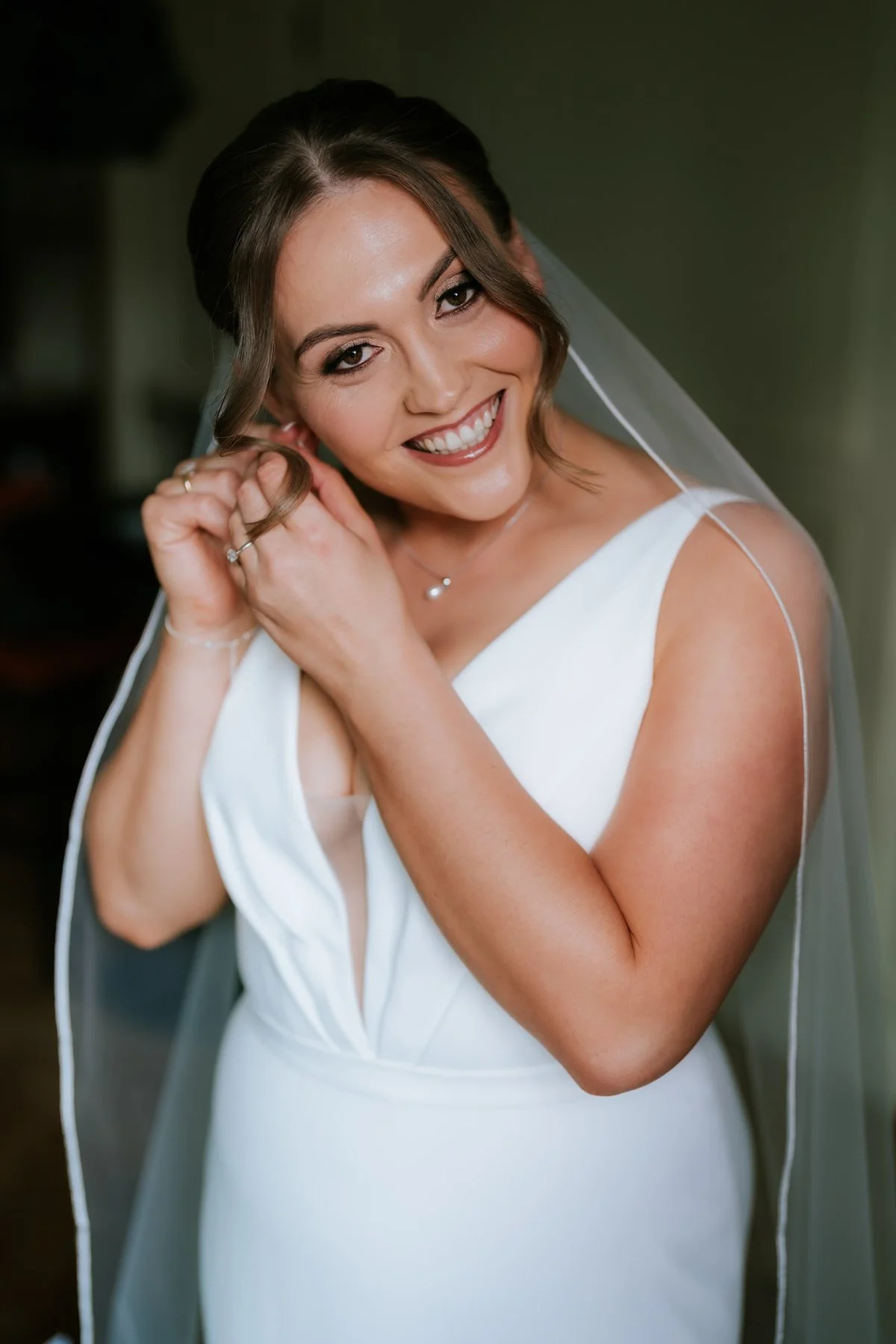 Kendall smiling as she puts on an earring in her wedding dress.