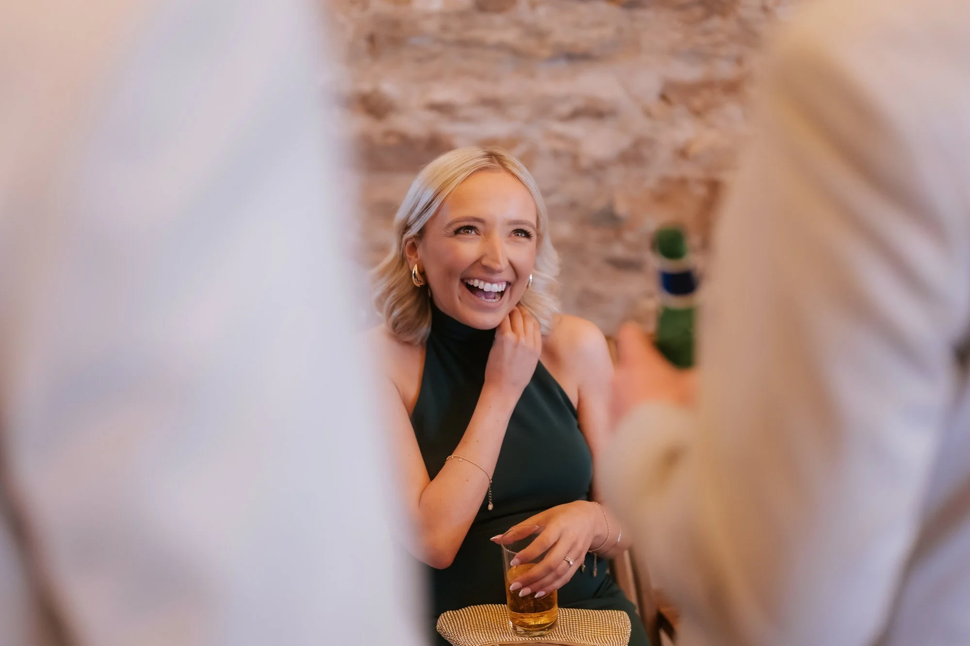 A blonde wedding guest laughing with a drink