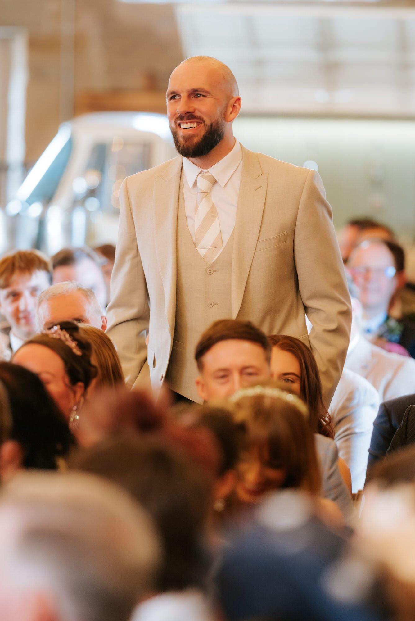 A bearded wedding guest in a cream suit smiling