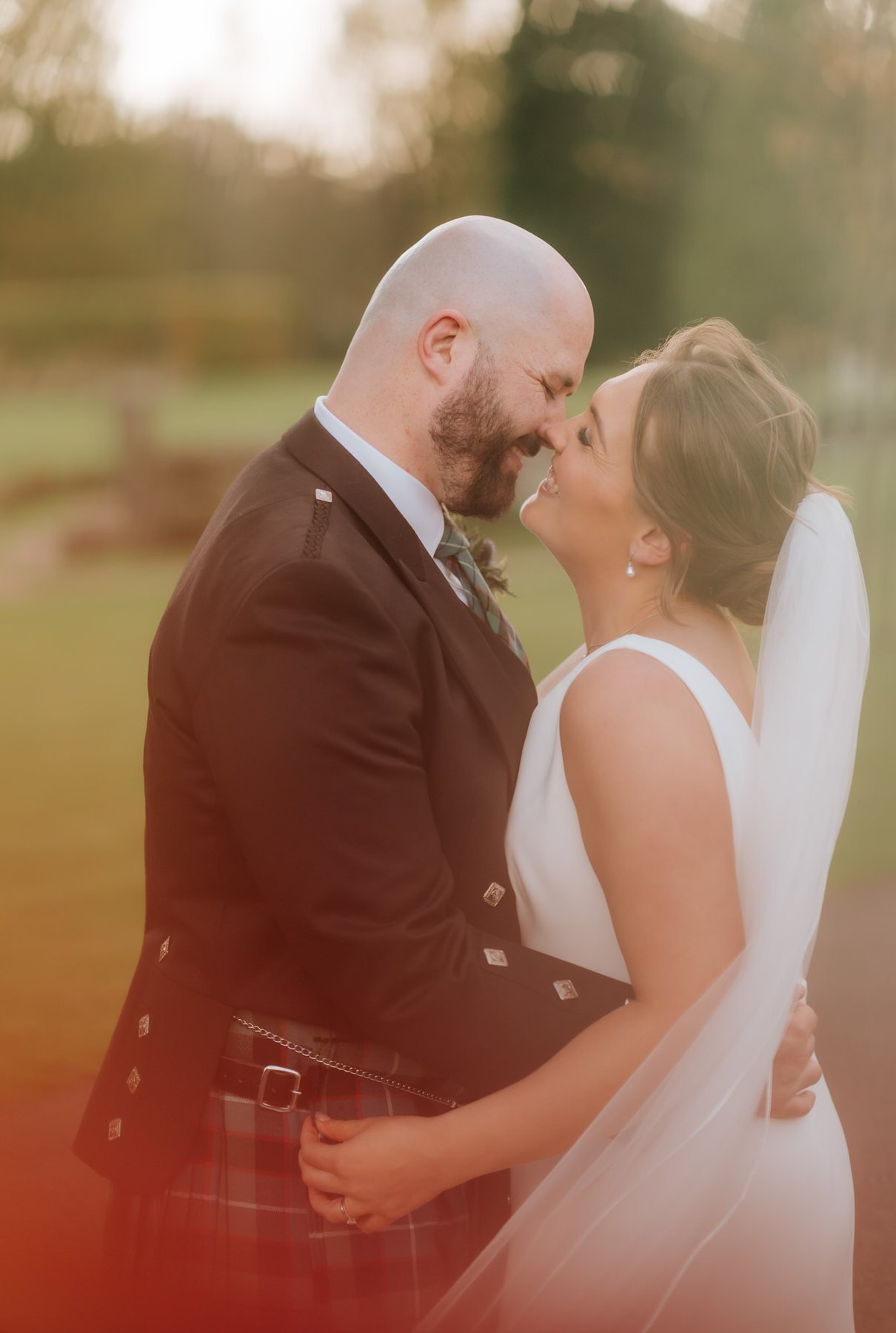 Kendall and Ewen sharing a kiss in warm October light among the trees.