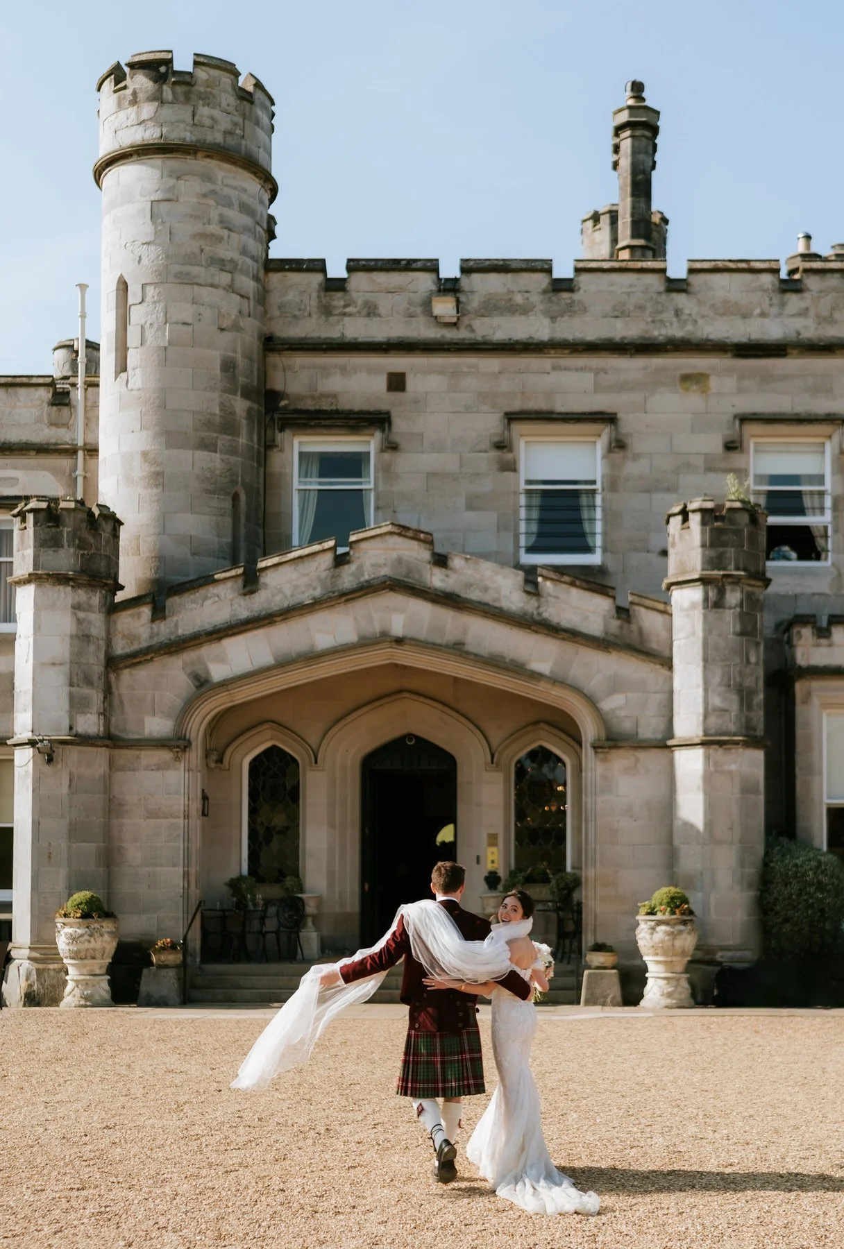 Kenneth lifting Kim in his arms in front of Dundas Castle’s stone entrance.