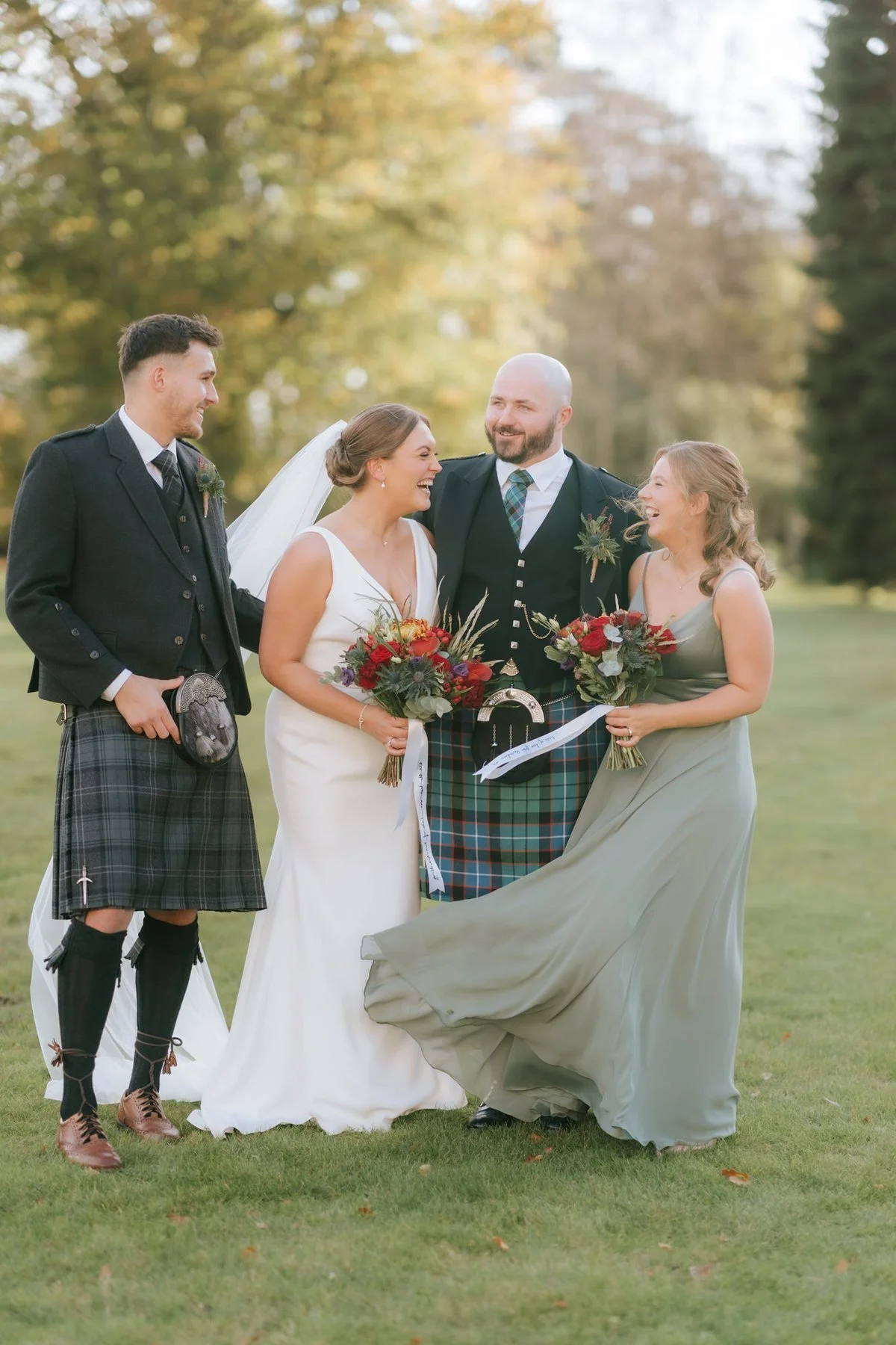Kendall and Ewen laughing with their wedding party on the lawn beneath autumn trees.