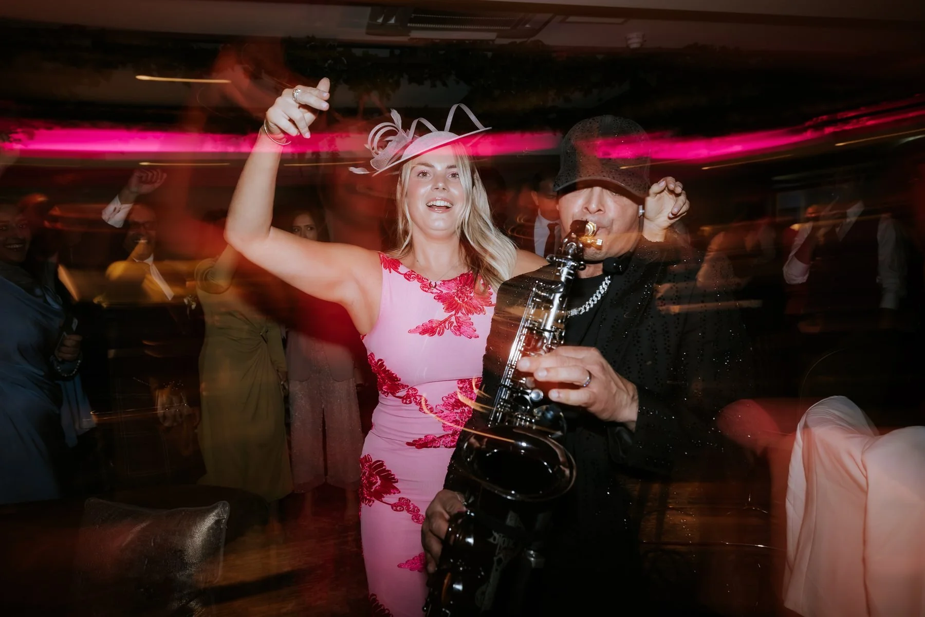 A guest dancing beside the saxophonist under colourful evening lights.