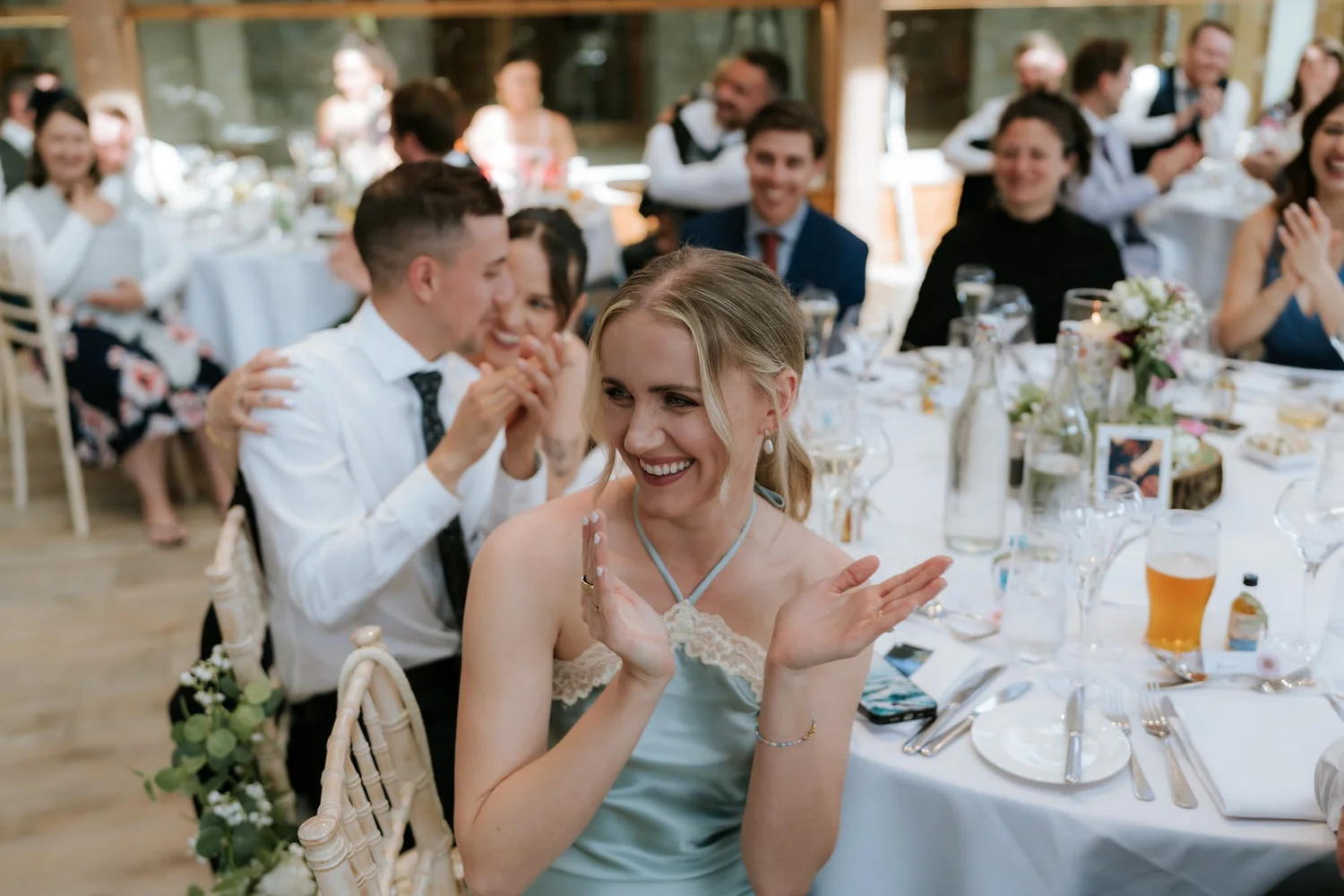 A bridesmaid clapping and laughing at her table during the wedding speeches.