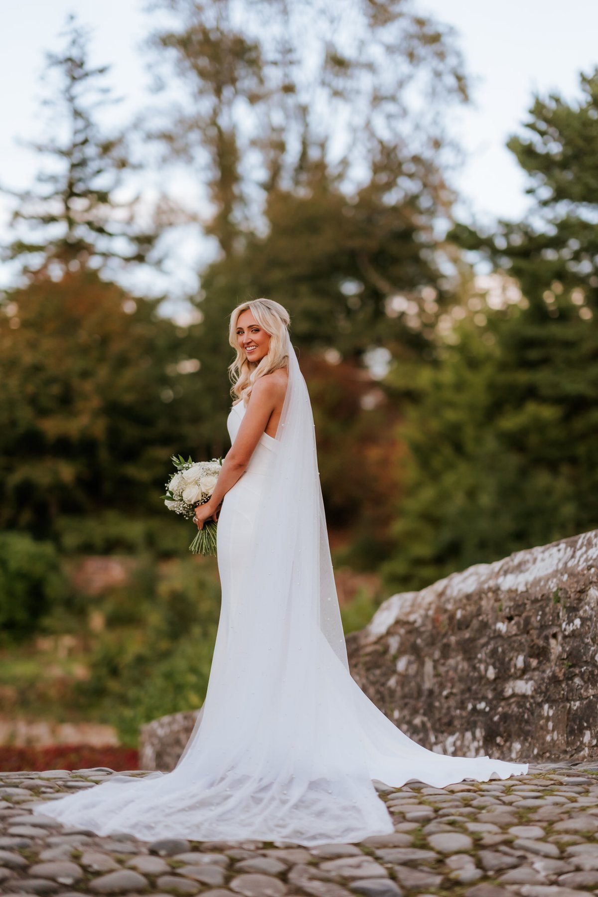 Lauren looking over her shoulder with her wedding dress spread across the bridge cobbles.