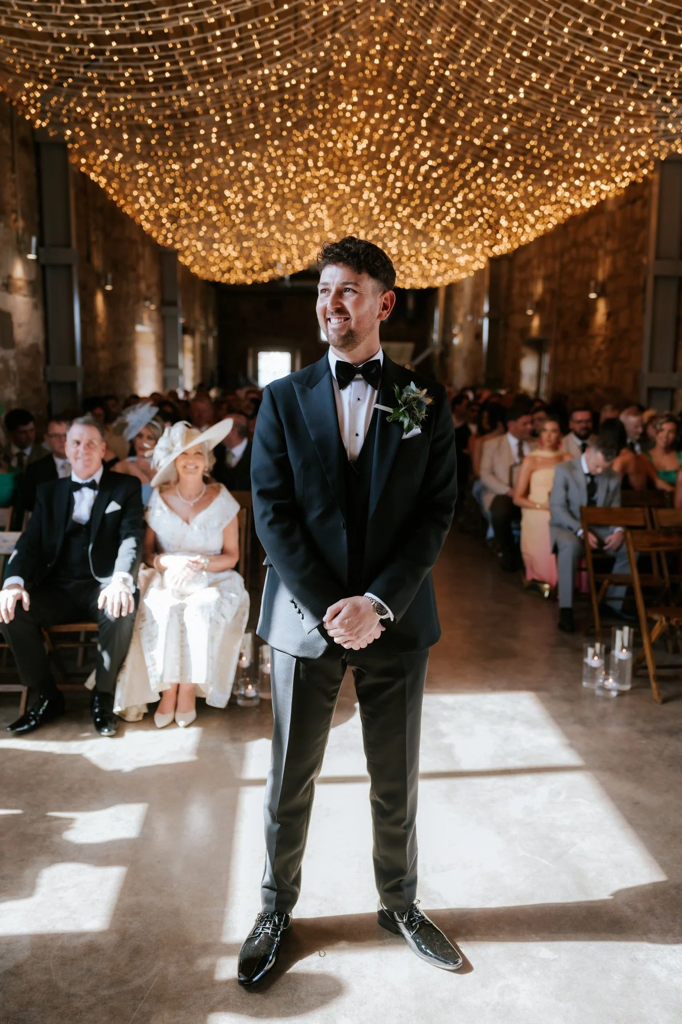 Jamie waiting beneath fairy lights in the ceremony room at Falside Mill