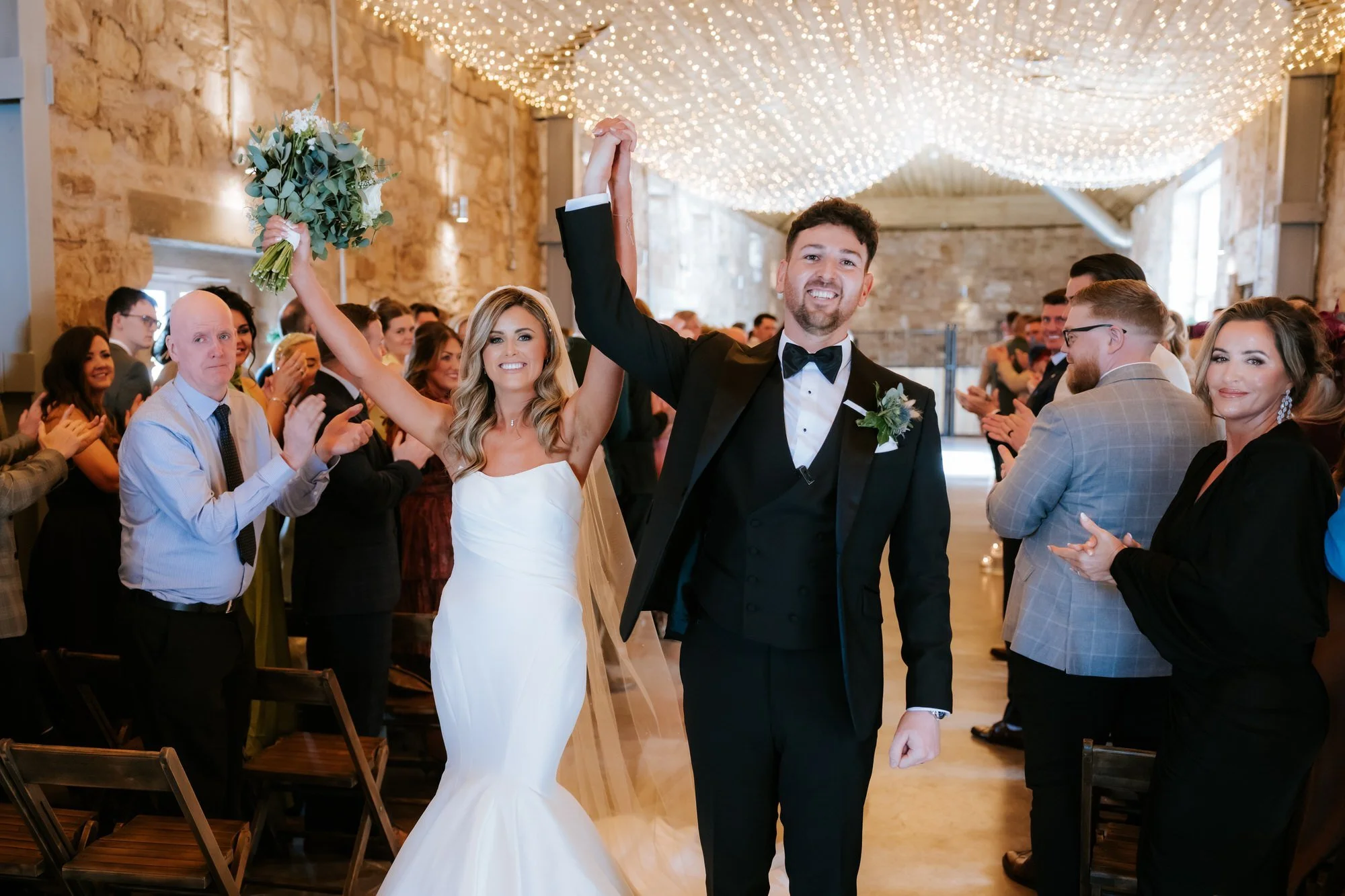 Natalie and Jamie raising their arms as they walk back down the aisle