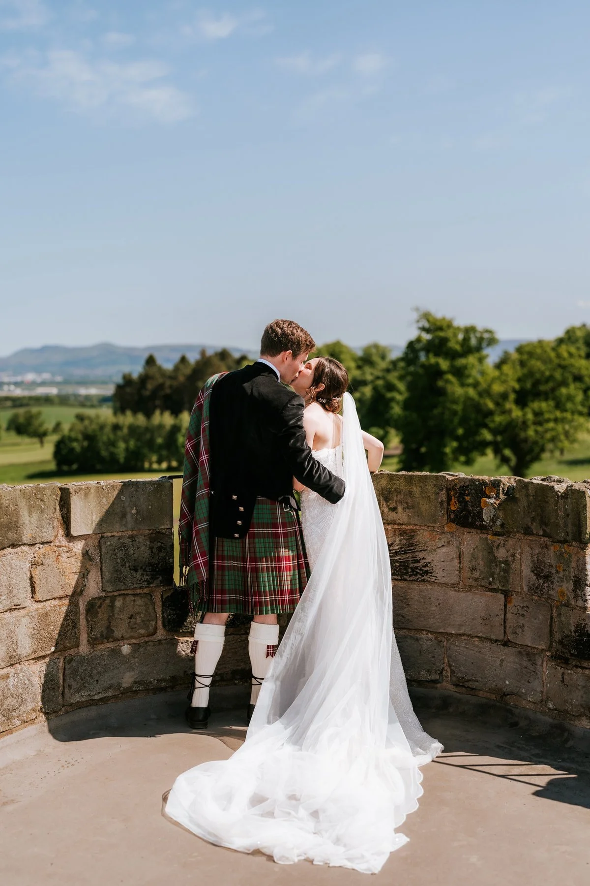 Kim and Kenneth kissing beside the rooftop battlements, with her veil trailing across the stone terrace.