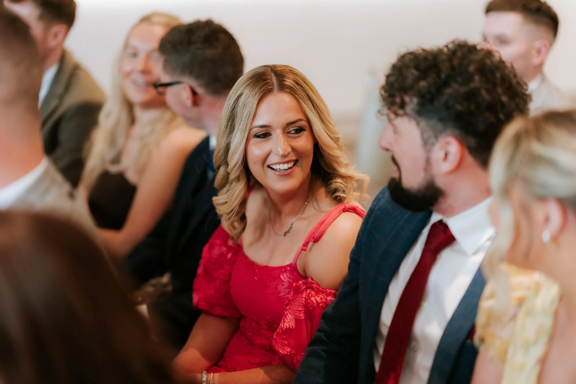 A guest in a red dress smiling towards the person beside her