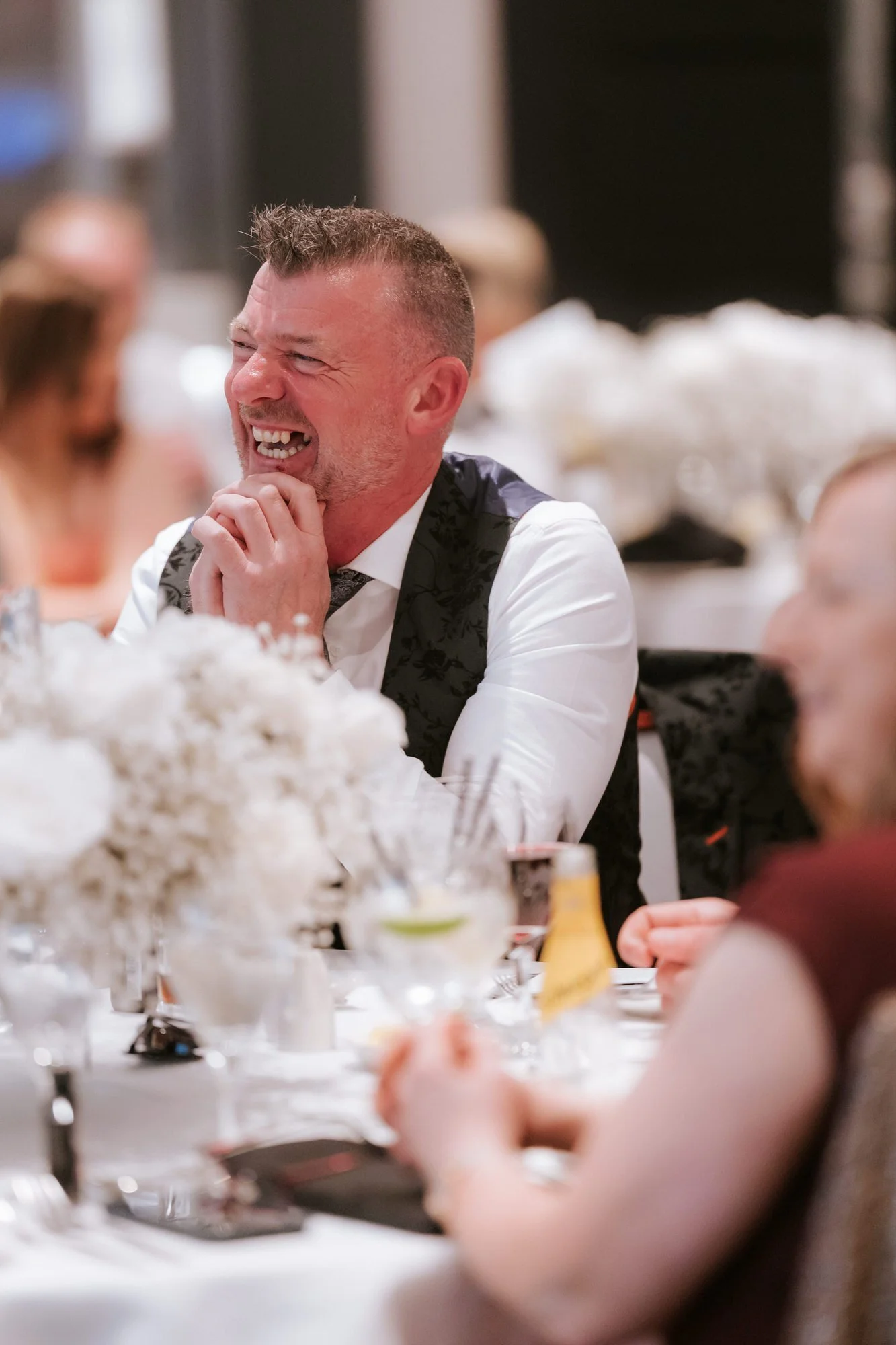 A guest in a patterned waistcoat laughing with his hands clasped