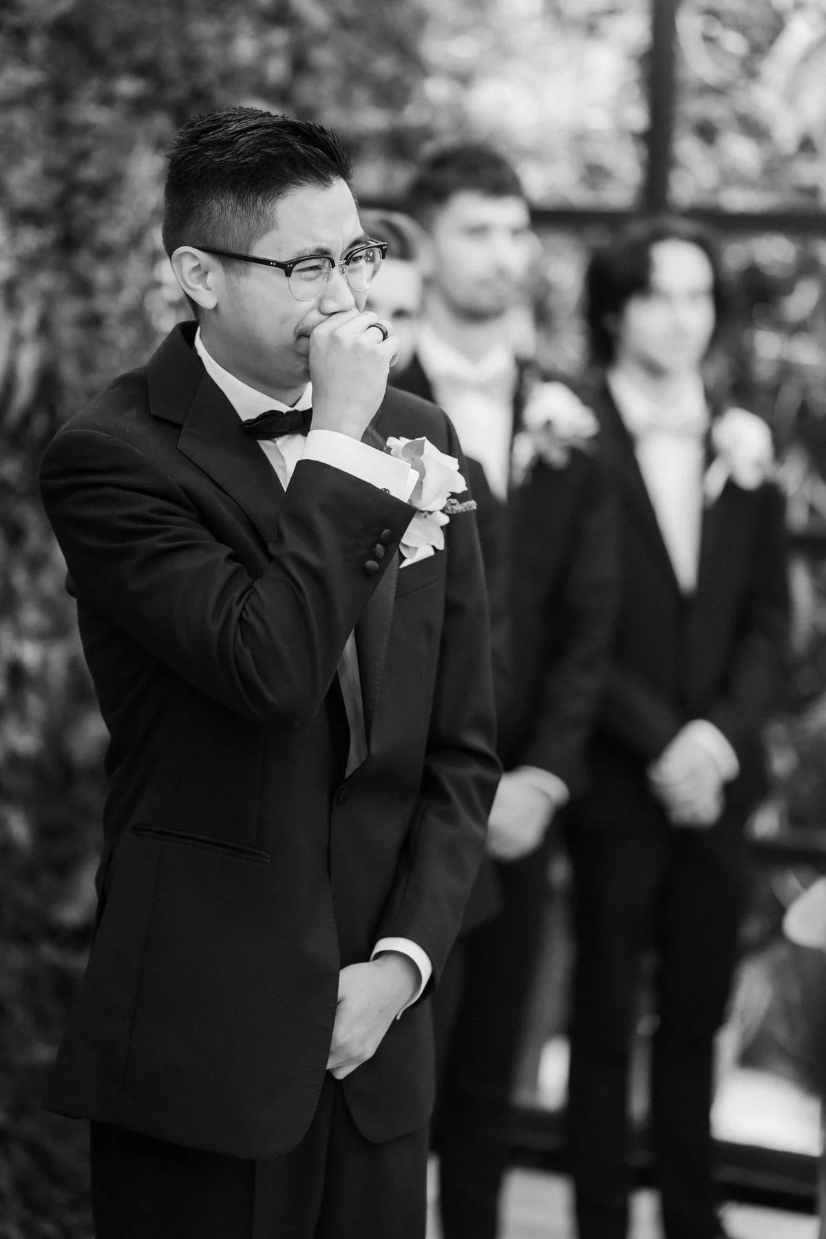 Carl smiling with his hand to his mouth during the wedding ceremony, photographed in black and white.
