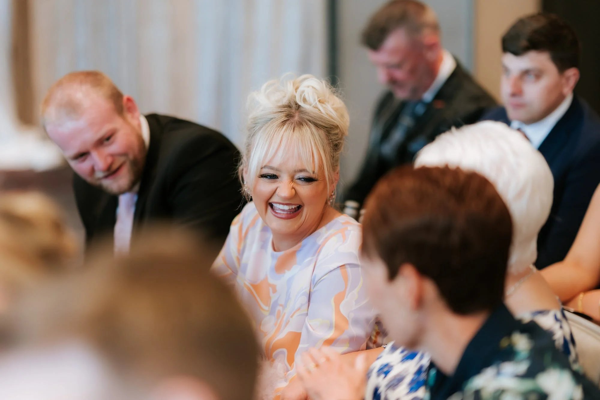 A wedding guest in an orange and lilac dress laughing during the ceremony