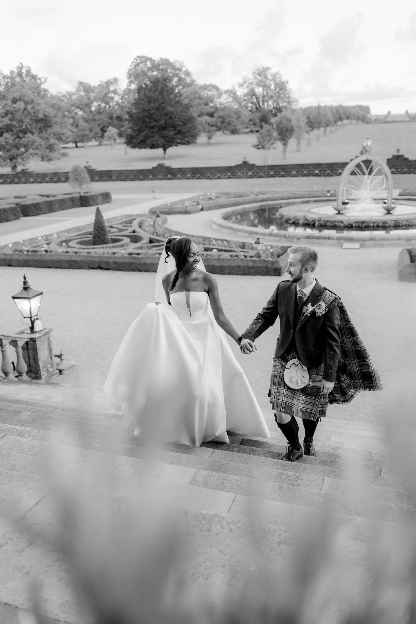 Kuda and Jamie holding hands on the steps with the formal gardens behind them.