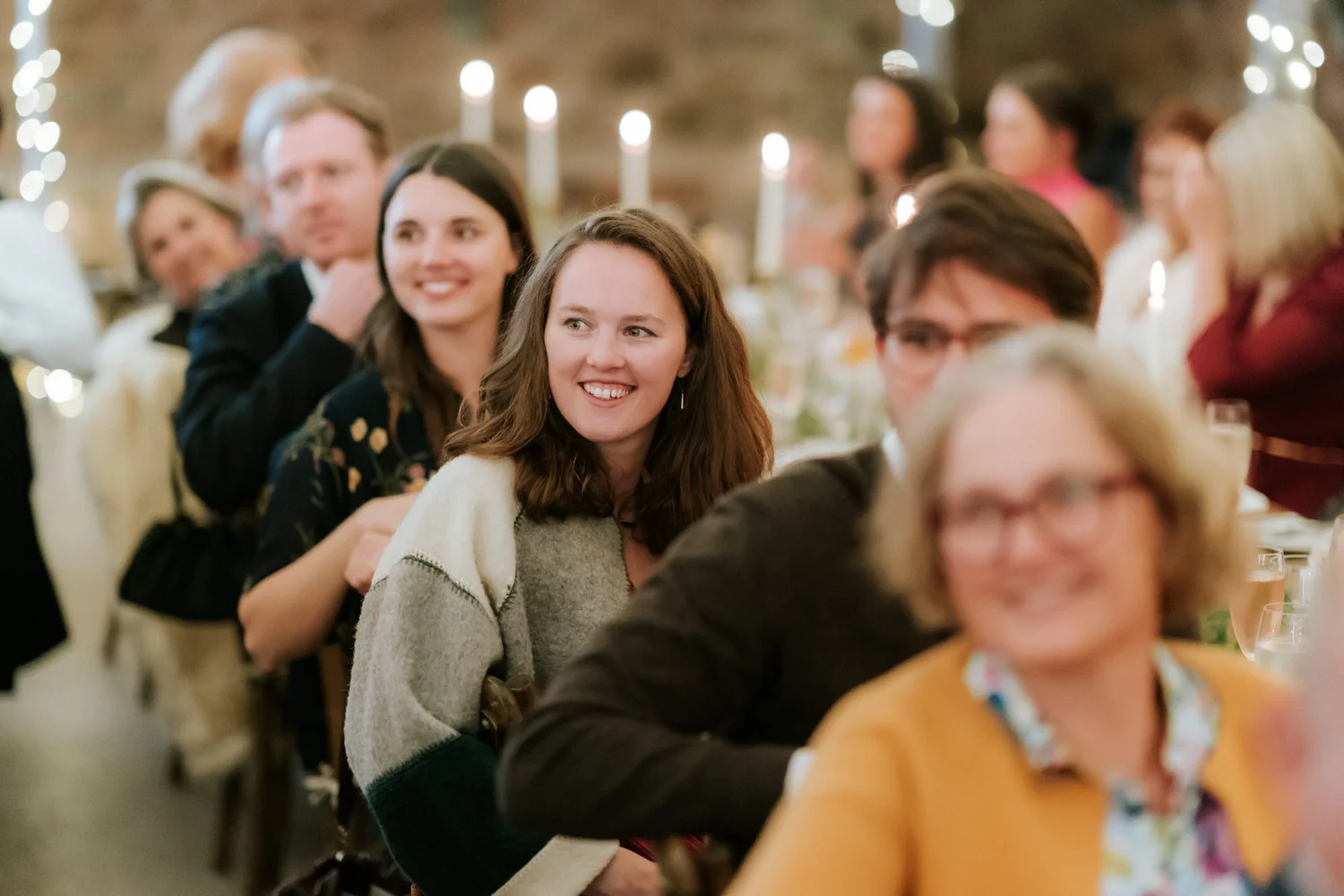Guests seated along the reception table smile towards the wedding speaker.