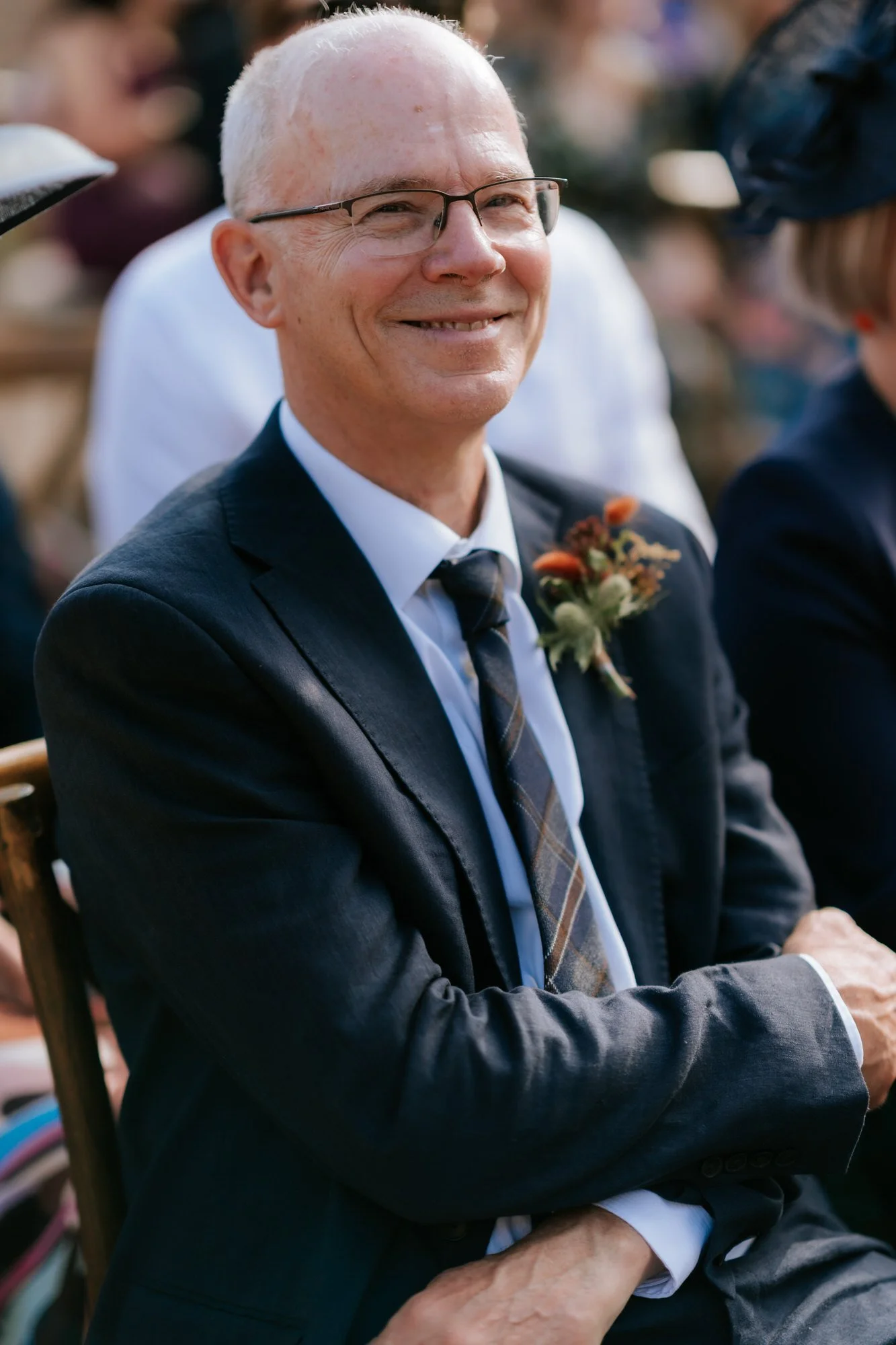 A guest wearing glasses and a dark suit smiles in the sunshine during the ceremony.