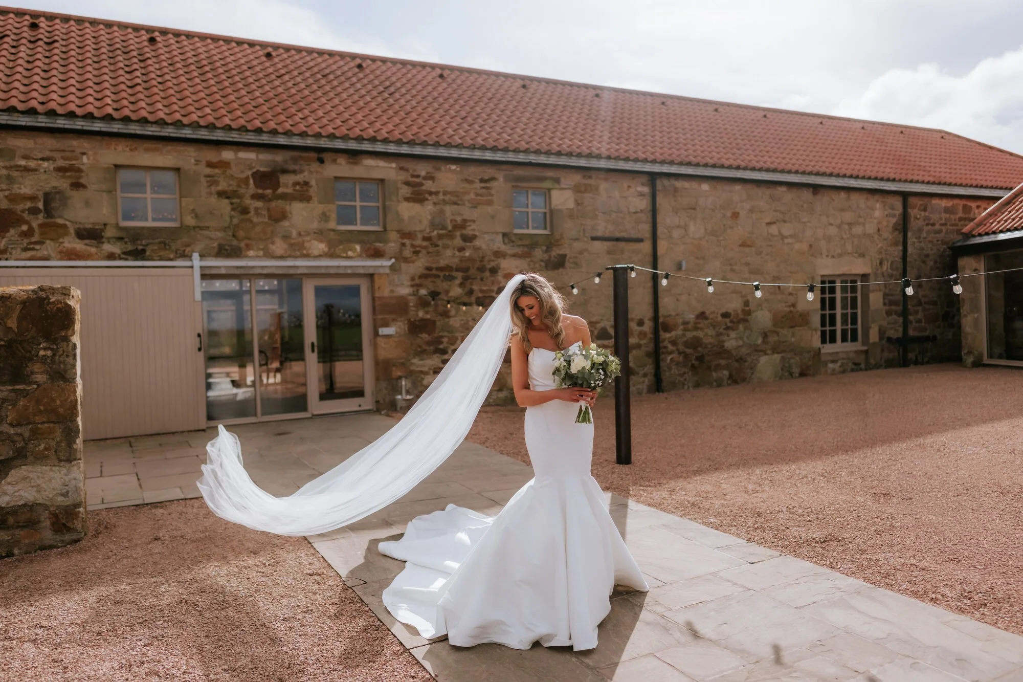 Natalie holding her bouquet as the wind lifts her veil