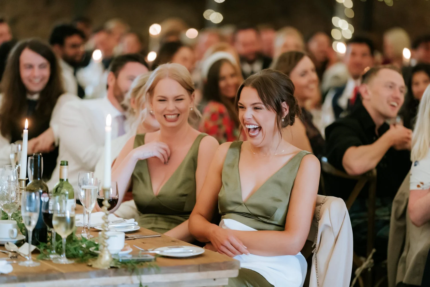Two guests in green dresses laugh together during the wedding speeches.