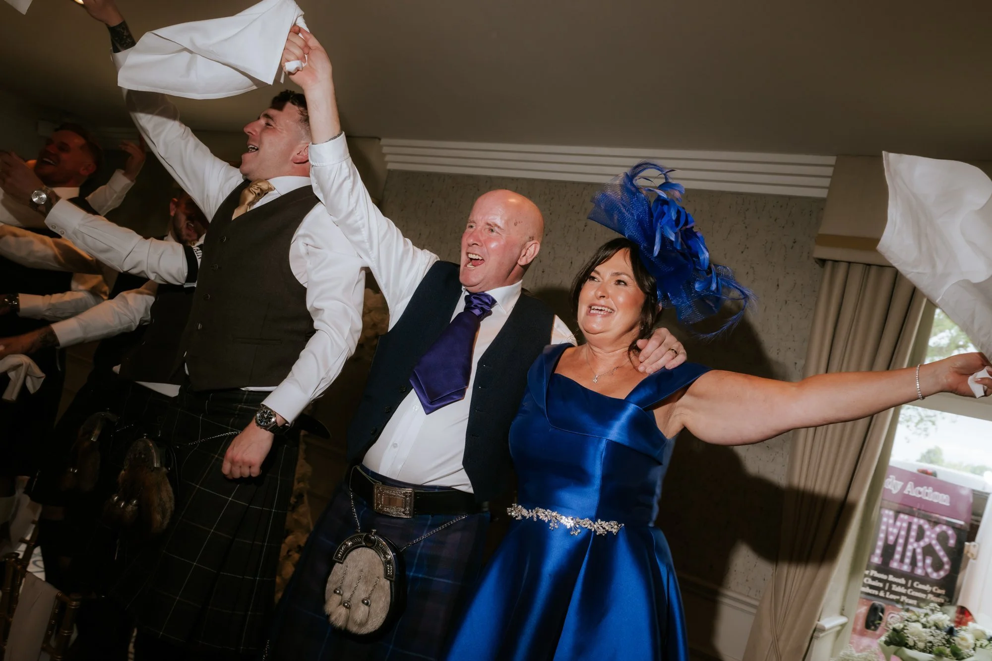 Wedding guests in blue waving napkins beside the top table at Glenbervie House.