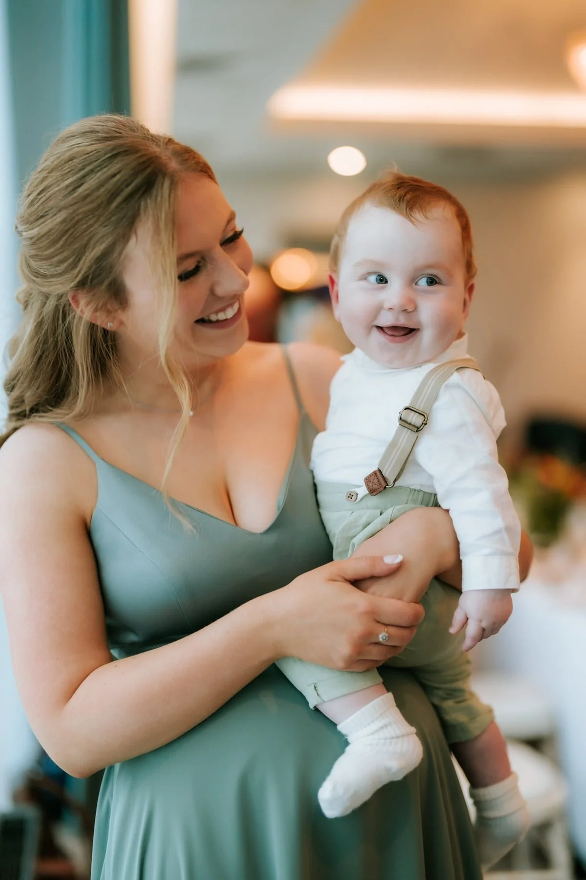 A guest in a green dress smiling while holding a baby at the wedding reception.