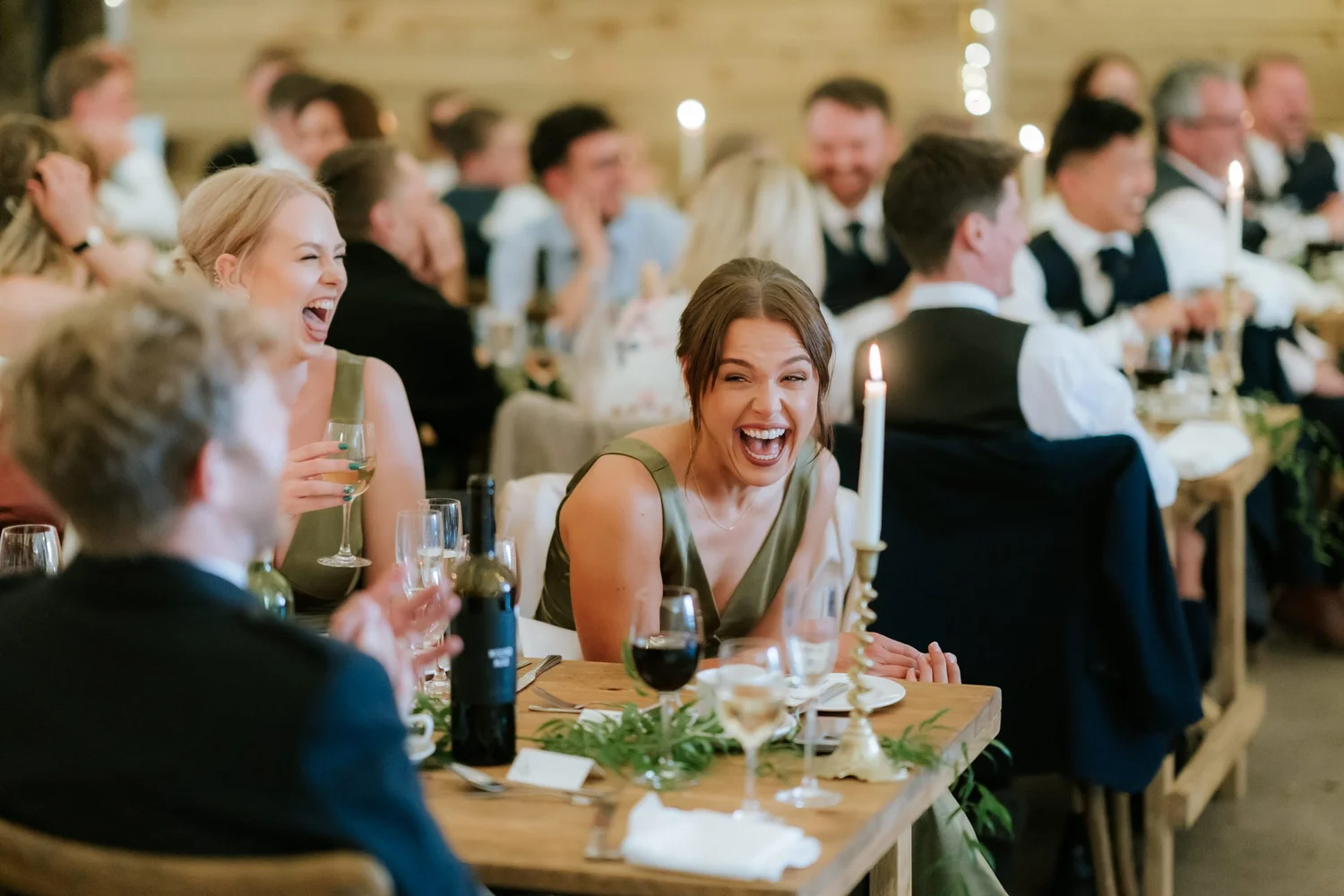 Guests in green dresses laugh together at a table decorated with candles and foliage.