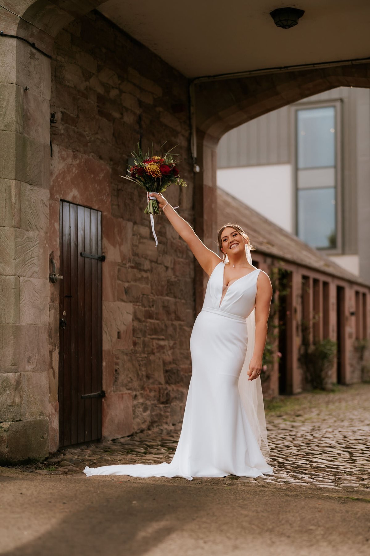 Kendall raising her autumn bouquet on a stone staircase at SCHLOSS Roxburghe.