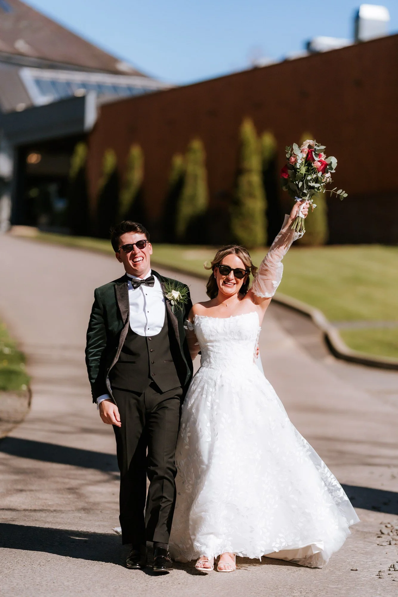 Ciara raising her bouquet beside Jonathon in the grounds.