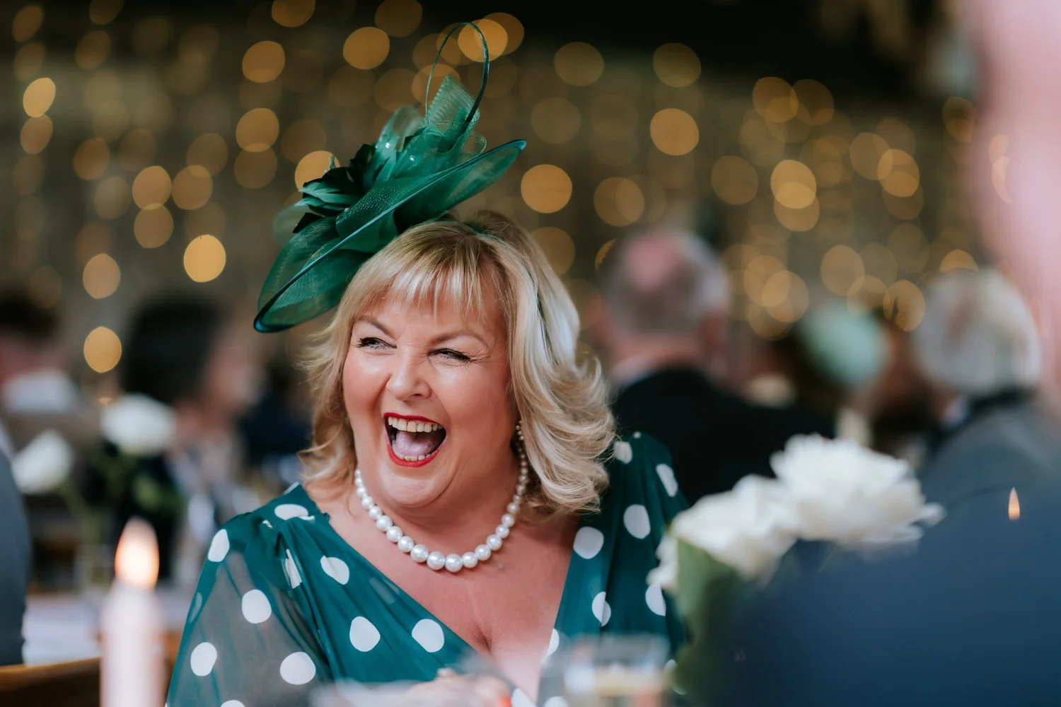 A guest in a green hat laughing during the wedding speeches.