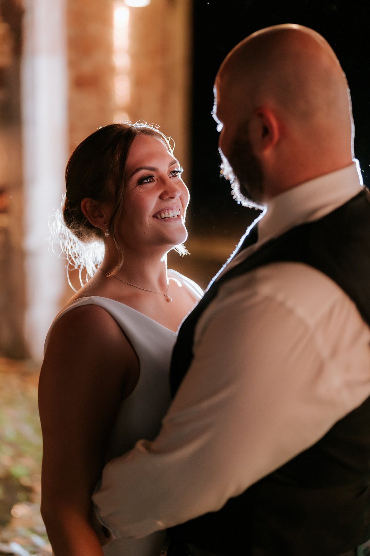 Kendall smiling up at Ewen in a warmly lit doorway during their evening portraits.